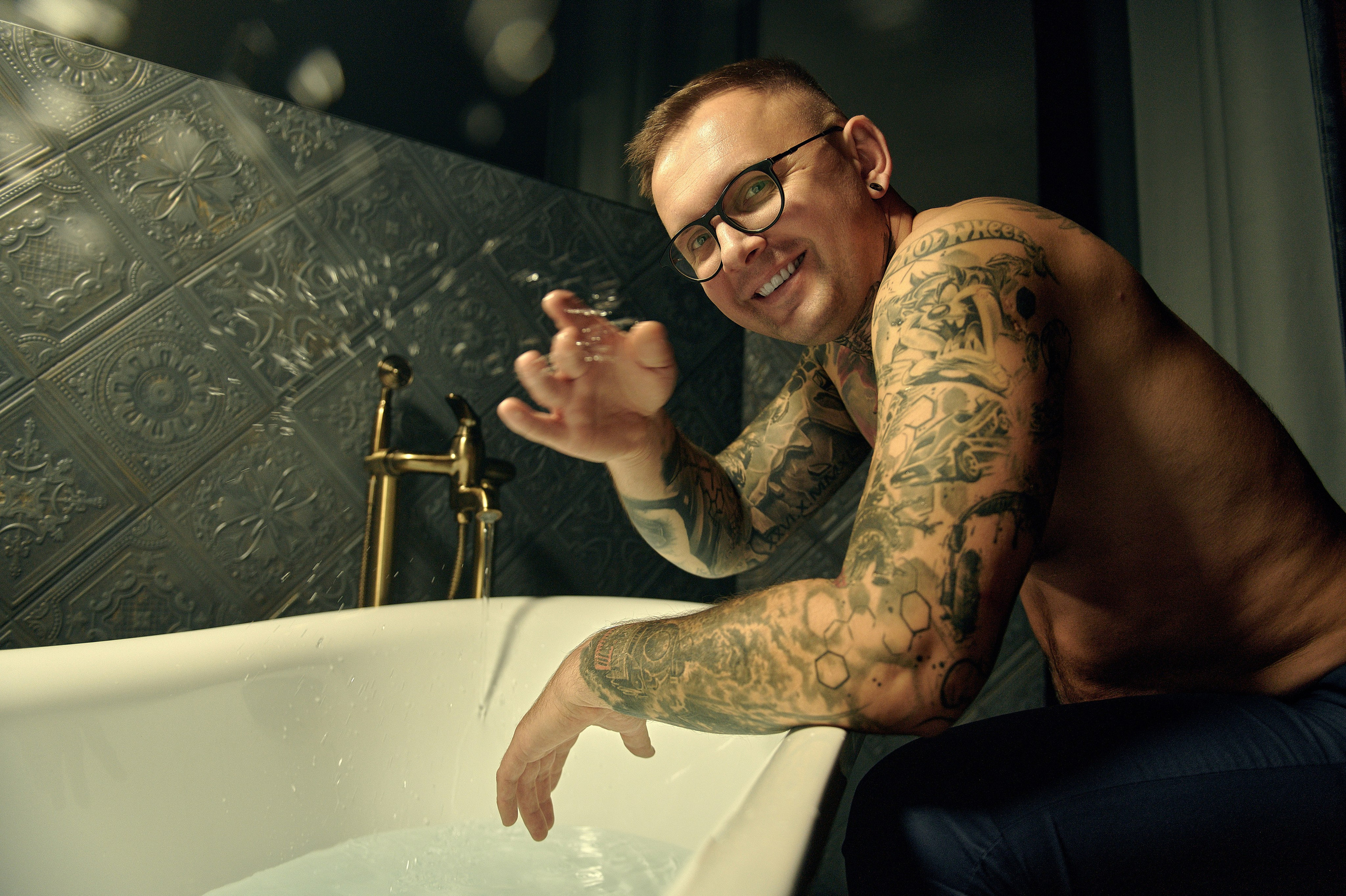 Uśmiechnięty mężczyzna z tatuażami chlapiący wodą przy wannie