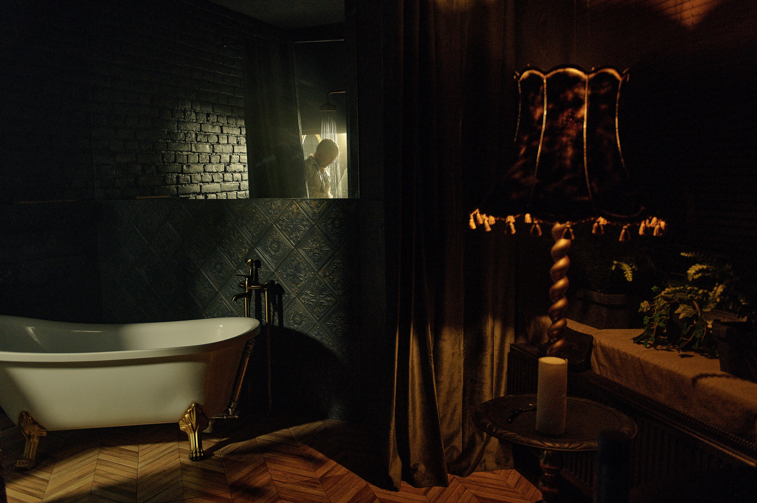 Klimatyczne wnętrze z wanną, zasłonami i lampą, w tle mężczyzna pod prysznicem