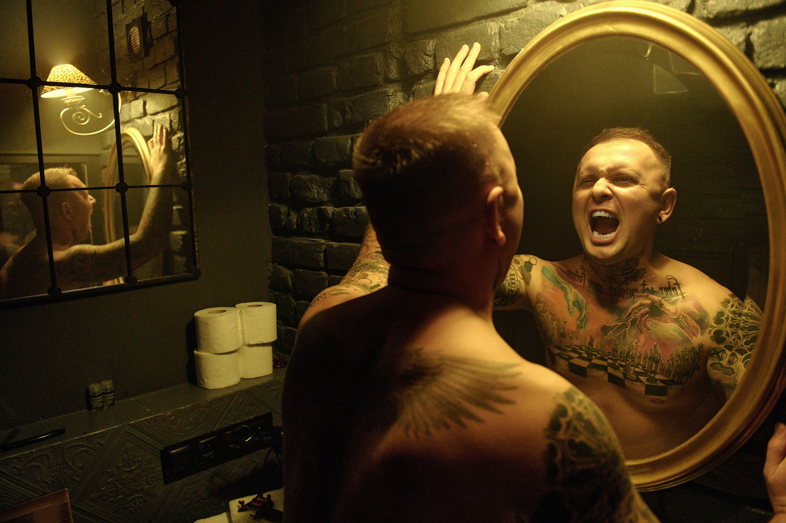 Mężczyzna bez koszuli krzyczy do lustra, odbicie pokazuje silne emocje