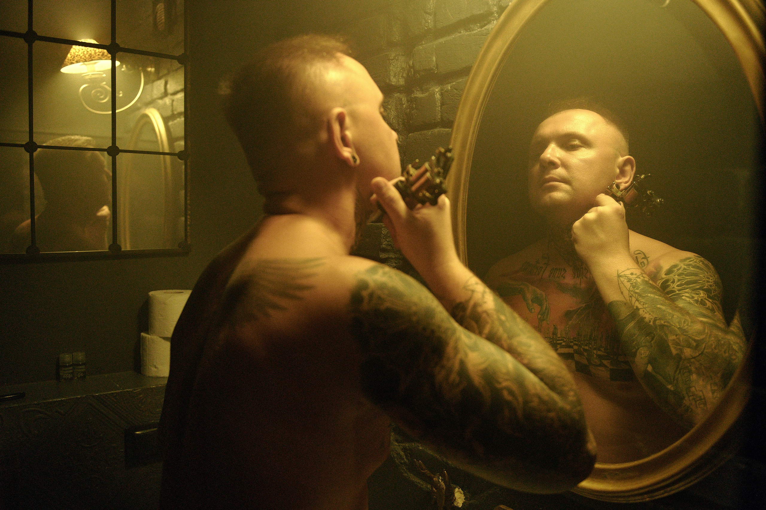 Mężczyzna bez koszuli patrzy w lustro i trzyma w ręku maszynkę do tatuaż