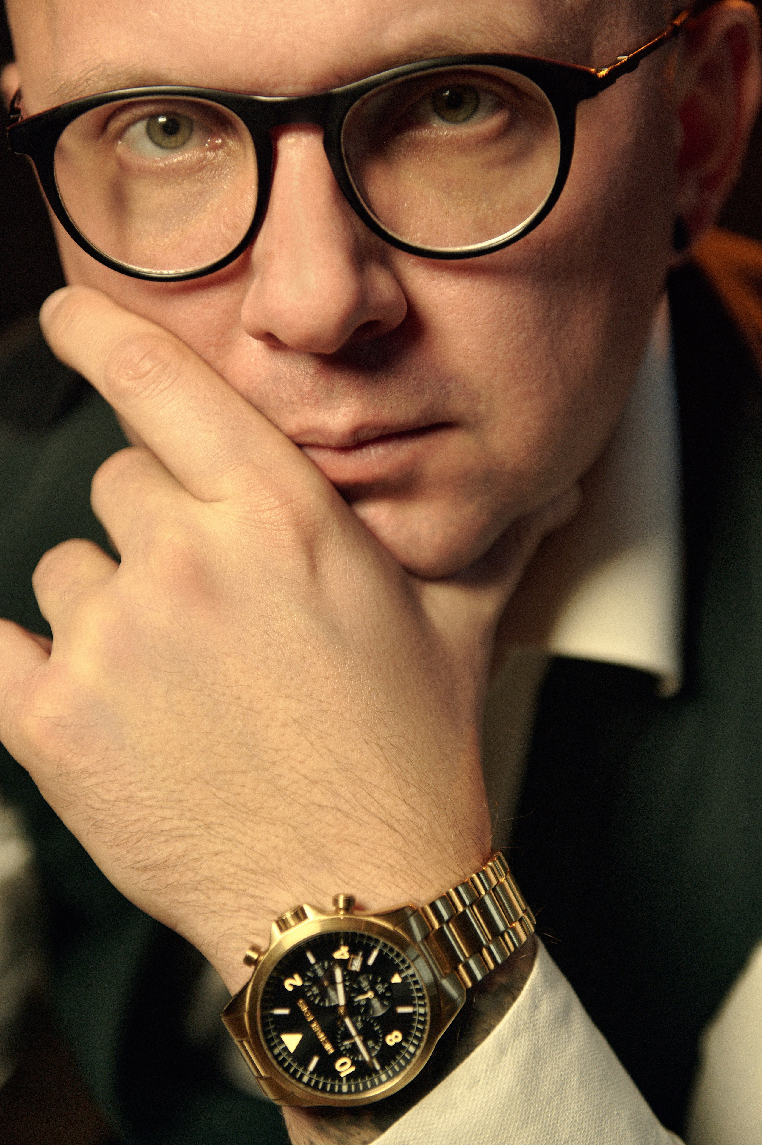 Mężczyzna z okularami patrzy prosto w obiektyw – zbliżenie, skupienie na spojrzeniu i złotym zegark