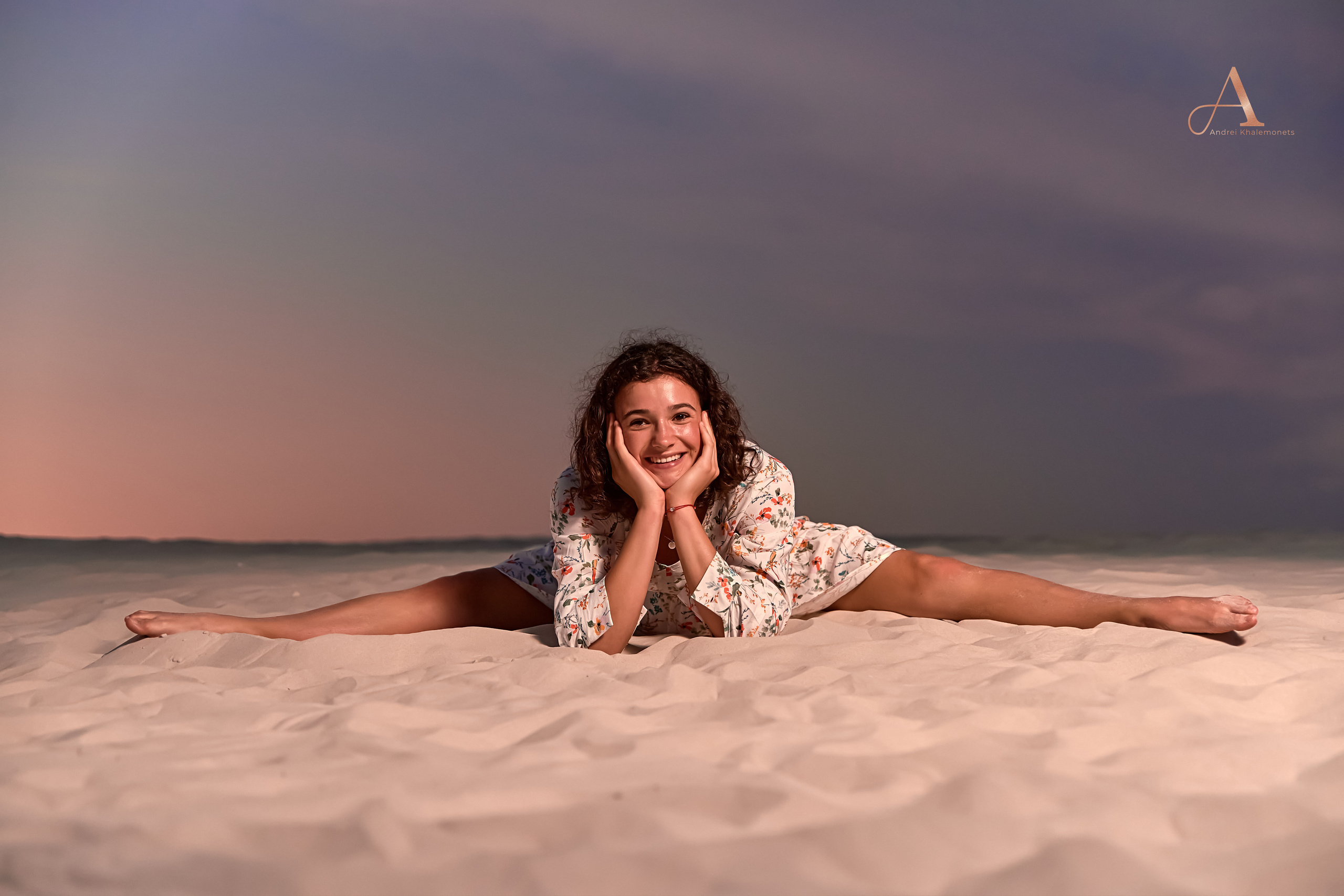 Девушка в коротком белом платье на песке в шпагате.