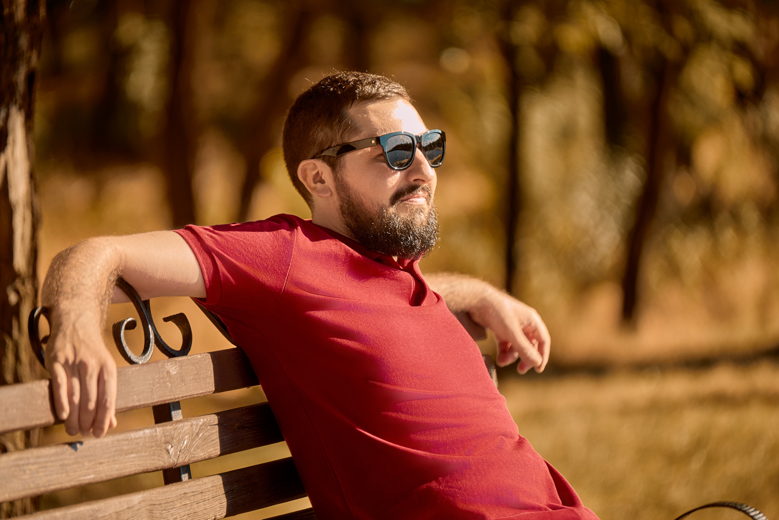 Парень в красном в парке на скамье в темных очках.