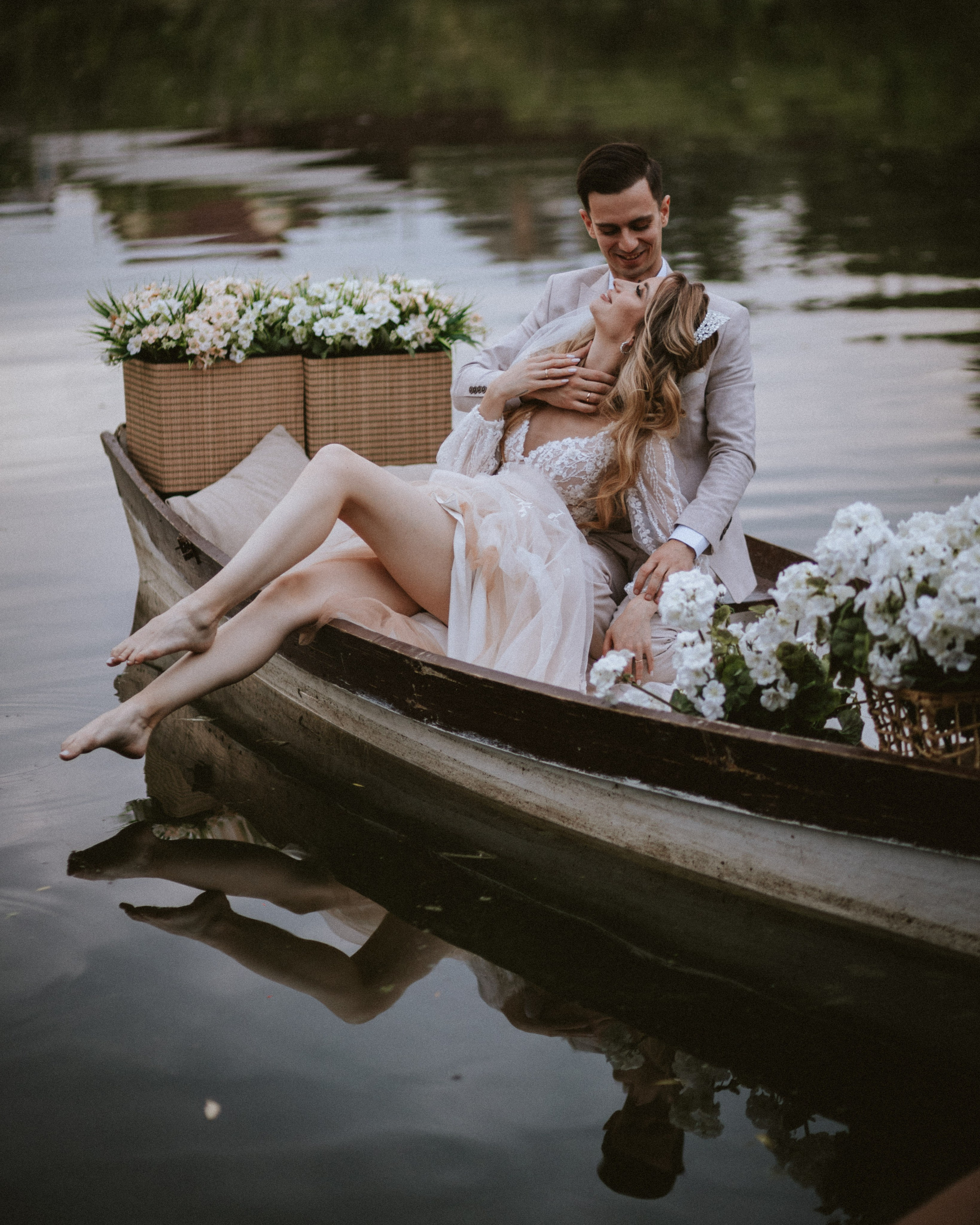 “The bride and groom enjoy the moment on a boat surrounded by flowers, with calm water in the background.”