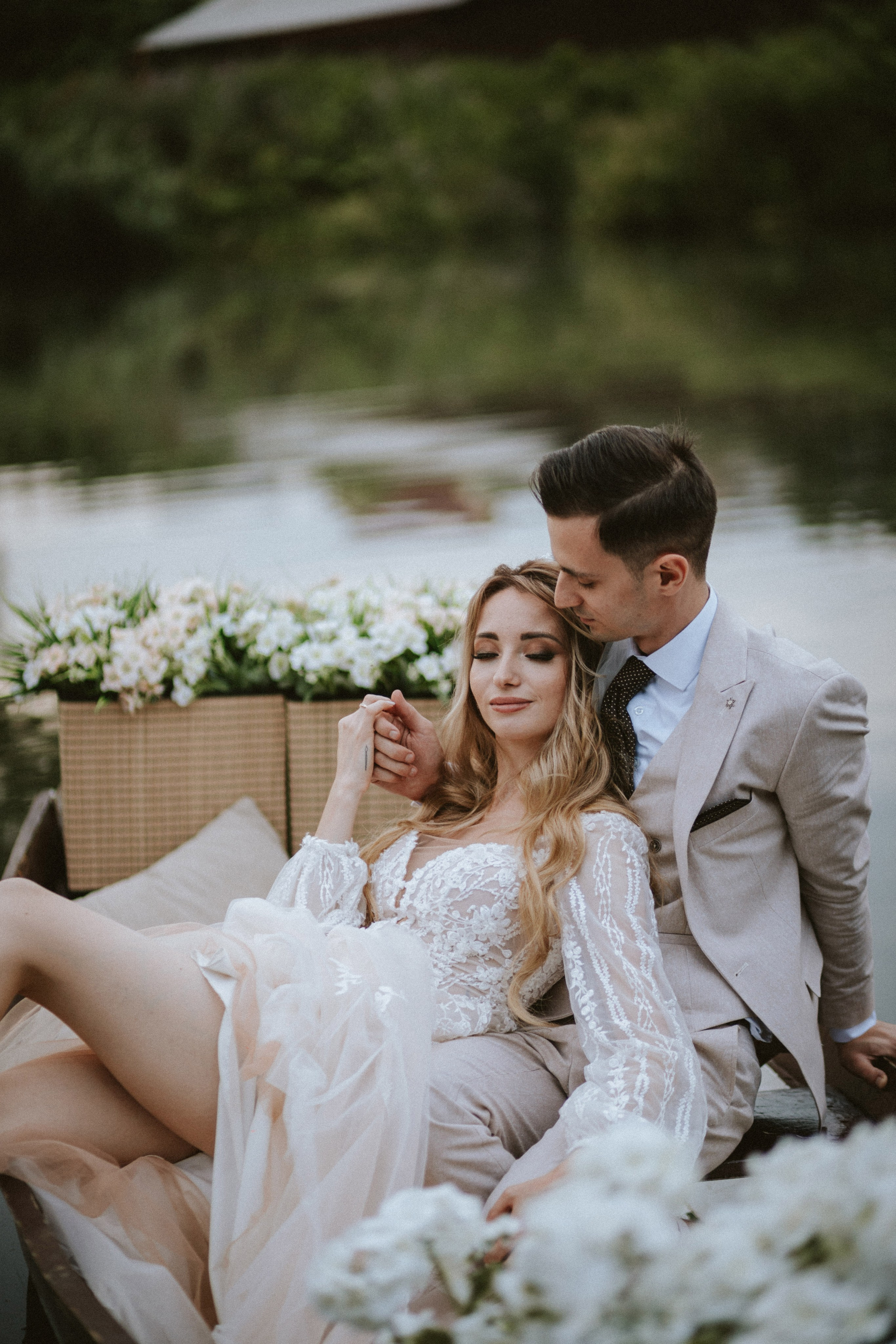 “Fotografo di matrimonio che cattura un momento romantico e sereno degli sposi su una barca, circondati da una vegetazione lussureggiante e fiori in fiore. La sposa, che indossa un elegante abito da sposa in pizzo, riposa tranquillamente tra le braccia dello sposo, creando un'immagine perfetta per un matrimonio di destinazione in Toscana.”