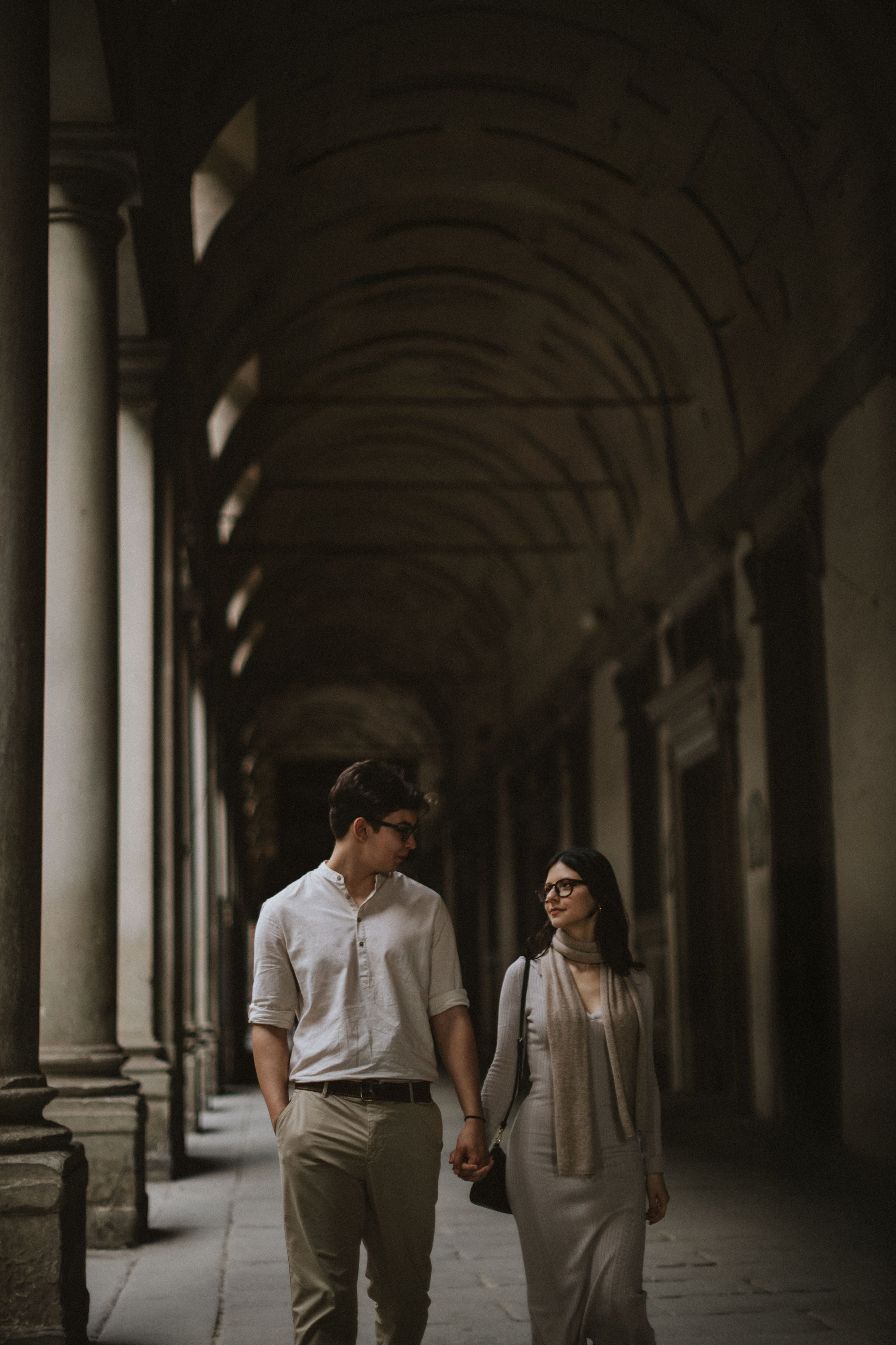 “Una coppia cammina mano nella mano lungo un bellissimo corridoio ad arco, sorridendosi a vicenda”.