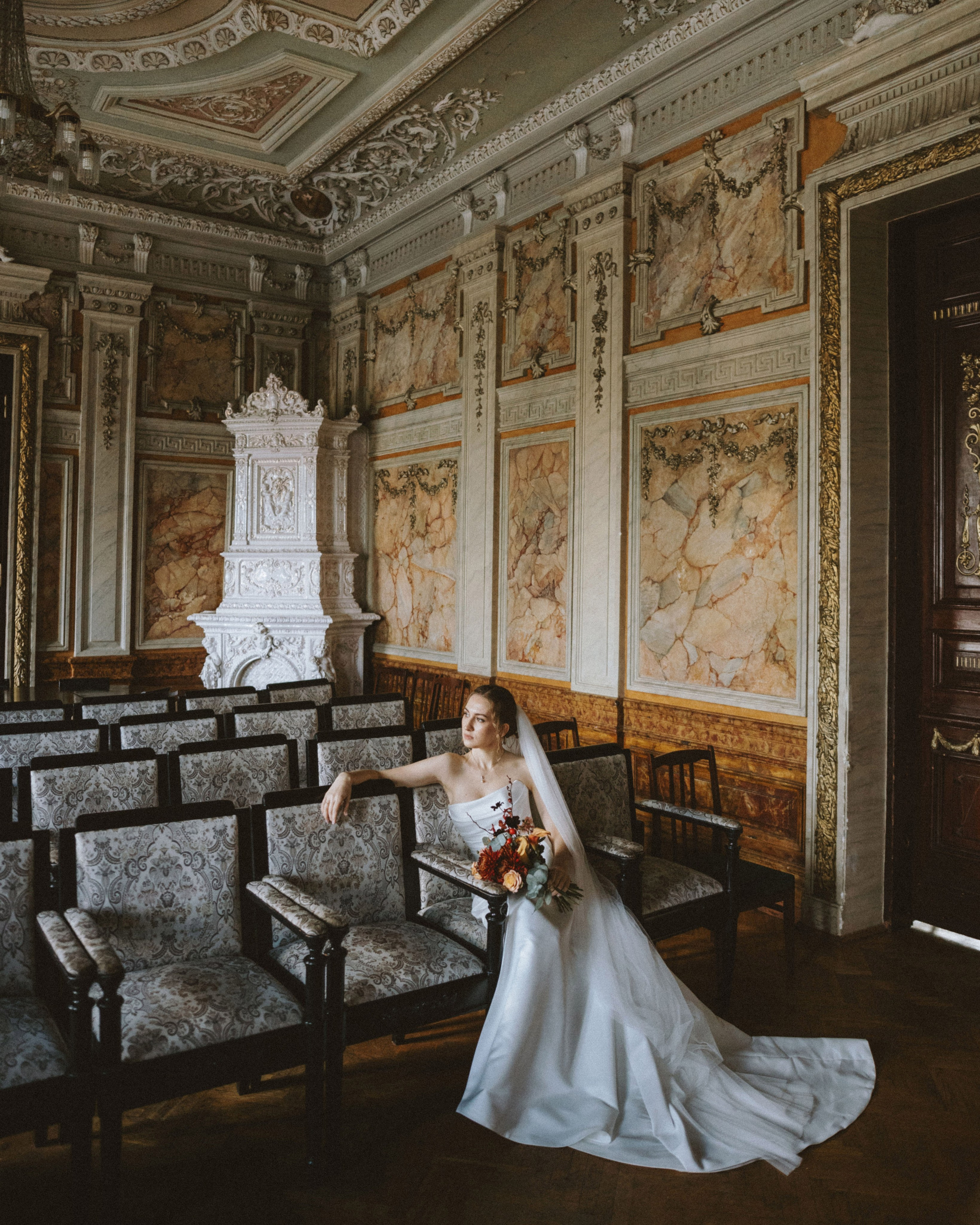 “The bride in a wedding dress sitting in a historic interior, surrounded by antique chairs and decorative walls in Italy, possibly in Rome or Milan.”