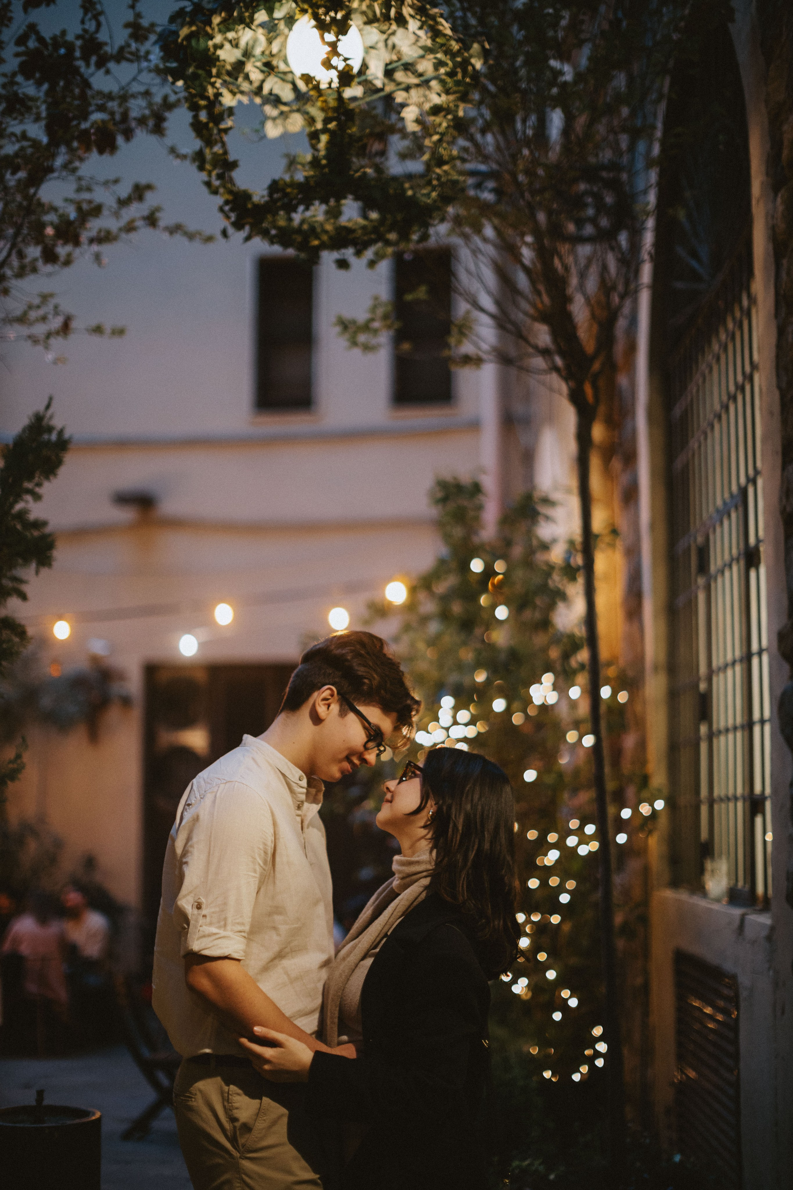“Una coppia che si abbraccia e si guarda in un ambiente accogliente, con luci soffuse, all'aperto”.