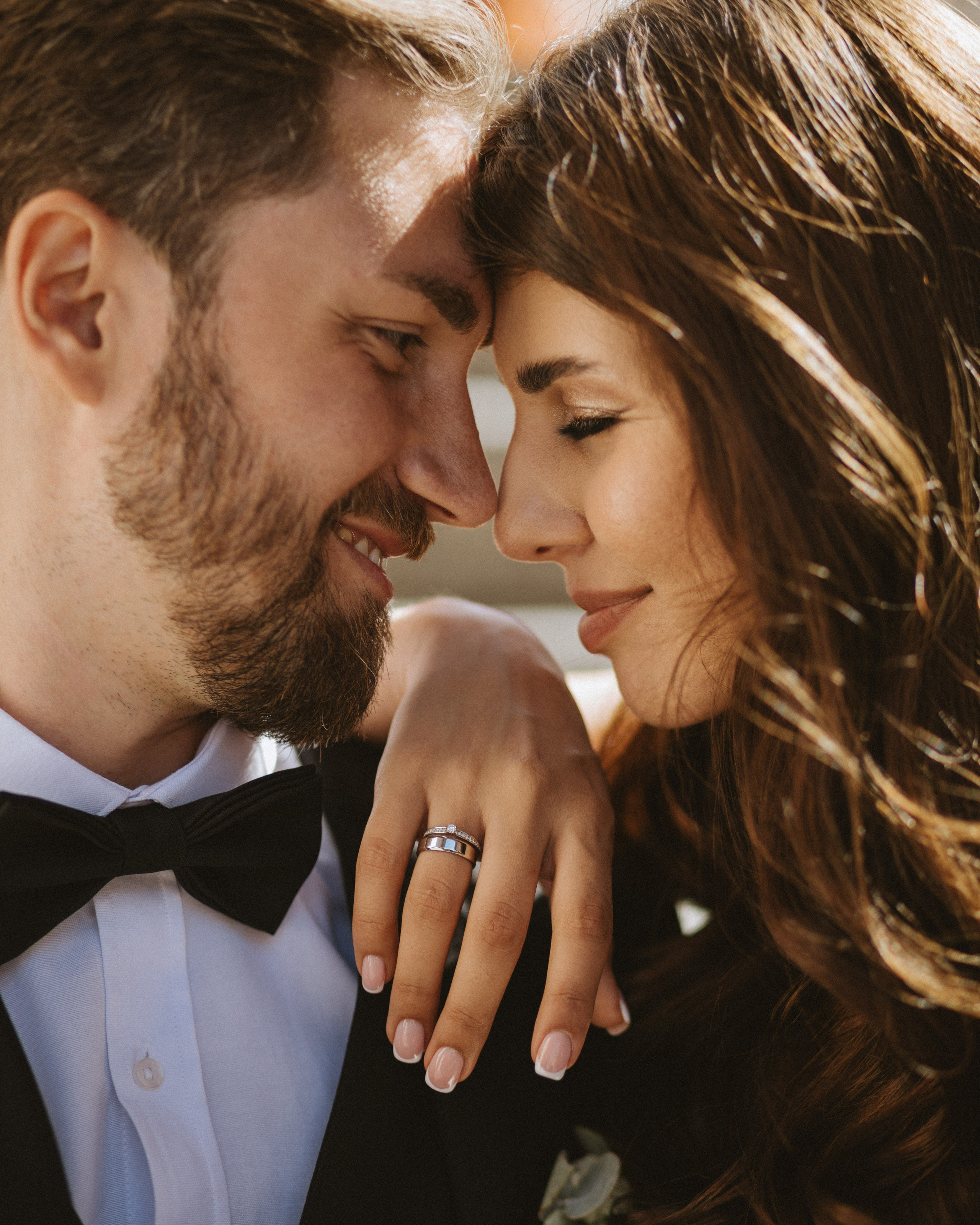 “Un primo piano di una sposa e di uno sposo che condividono un momento di intimità mentre appoggiano la fronte l'uno all'altro, guardandosi negli occhi. La mano della sposa poggia delicatamente sul petto dello sposo, mettendo in mostra la fede nuziale, mentre entrambi irradiano amore e felicità. Le loro espressioni facciali trasmettono un affetto e una gioia profondi, sottolineati dall'illuminazione naturale che esalta il loro legame”.