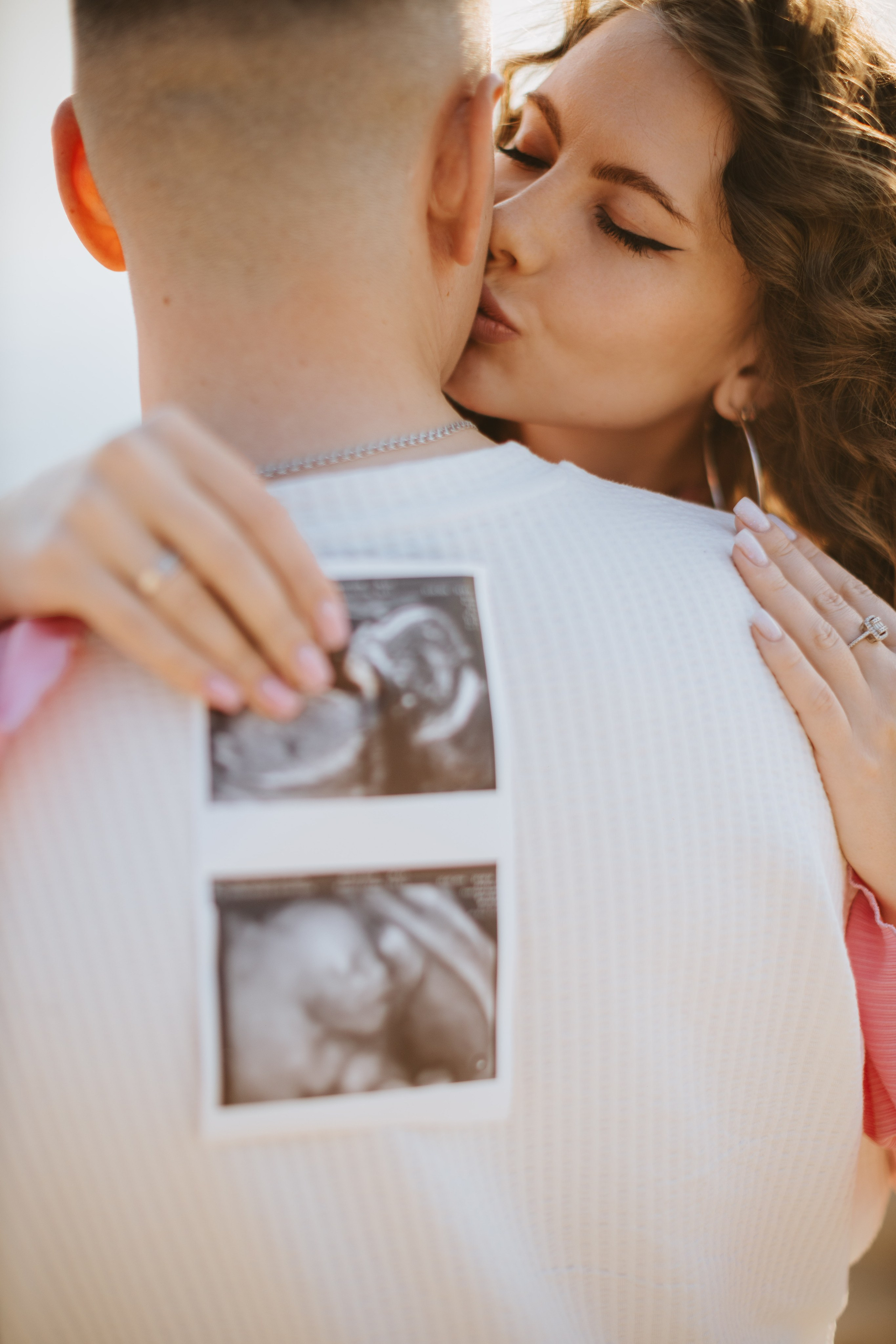 “Una donna che bacia la schiena del suo partner mentre lo tiene da dietro. Sulla camicia dell'uomo c'è l'ecografia del loro bambino, che aggiunge un tocco personale al momento. La foto cattura il loro legame intimo e affettuoso, circondato da una luce soffusa”.