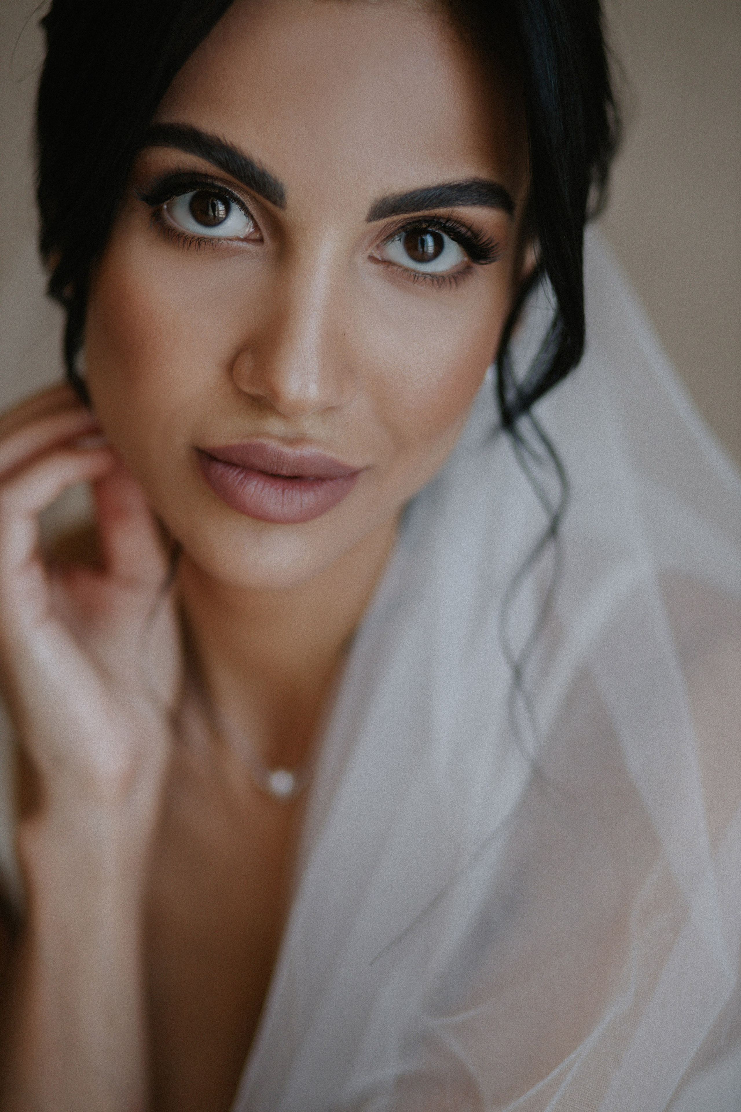 “Primo piano della sposa, che cattura l'eleganza nei suoi occhi mentre tocca delicatamente il suo velo. Il trucco morbido, la collana delicata e la bellezza naturale rendono questo momento di grazia nuziale senza tempo”.