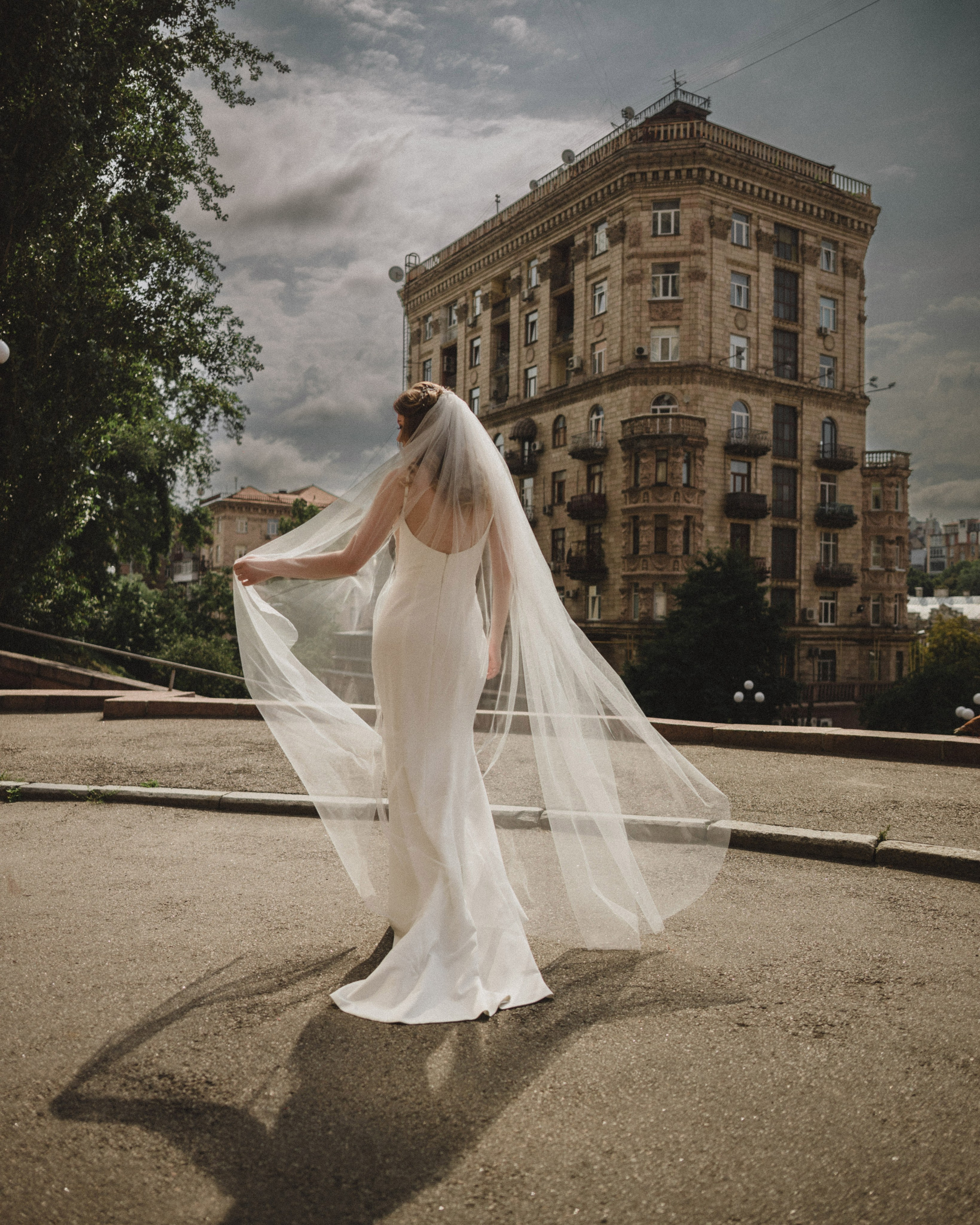 “The bride in a white dress with a flowing veil against the backdrop of a historic building, a wedding in one of Italy’s major cities, possibly in Milan or Rome.”