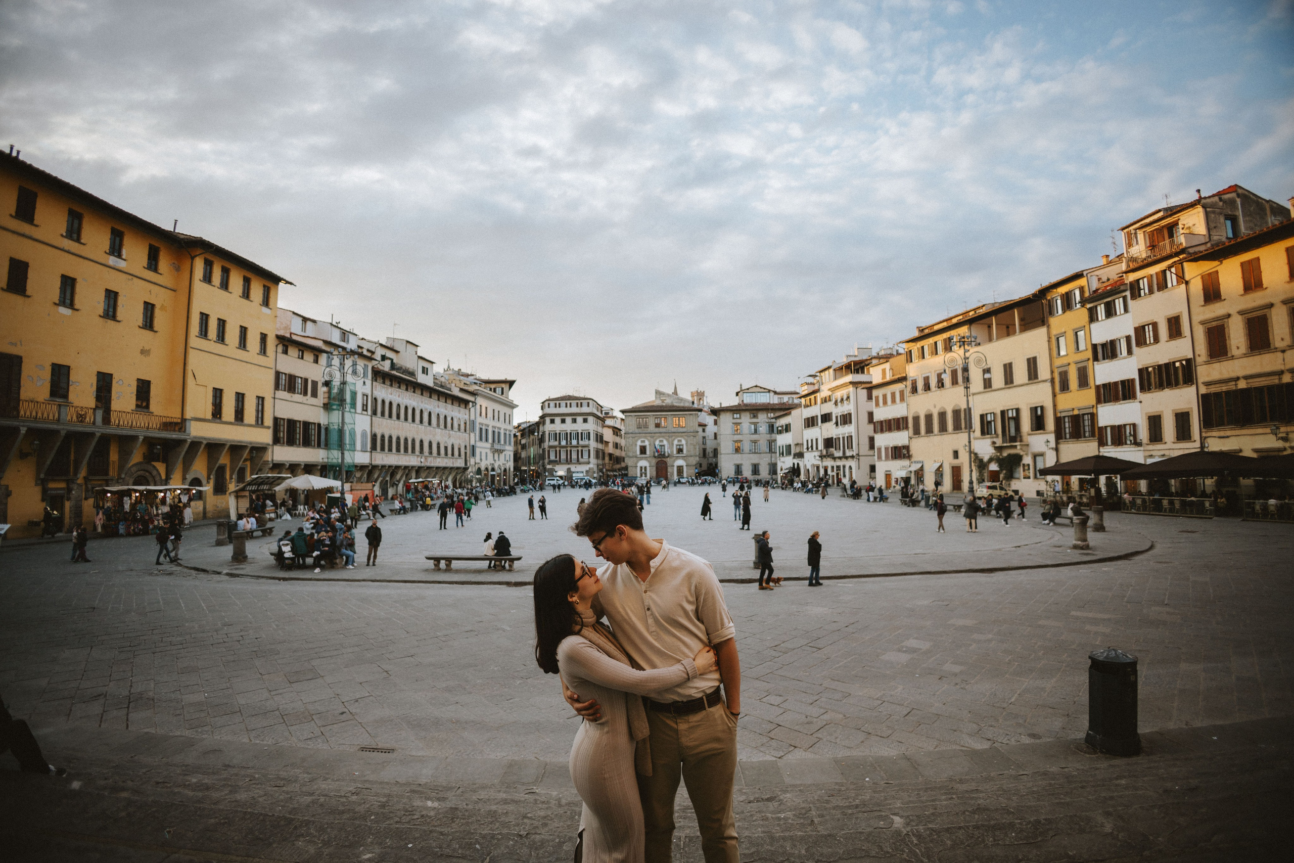 “Una coppia che si scambia un bacio in una piazza vivace con edifici colorati intorno a loro”.