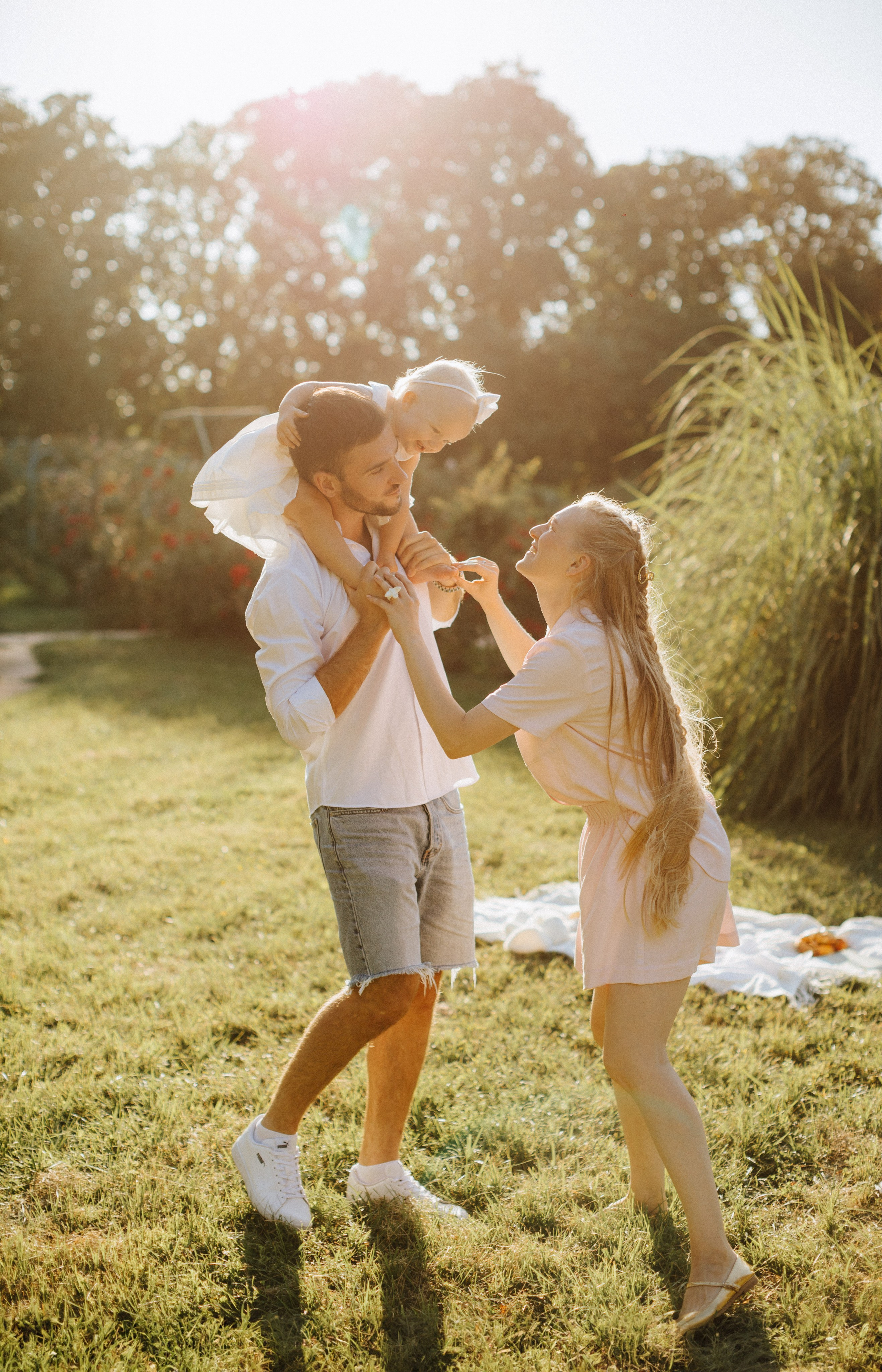 “Una famiglia gioiosa che trascorre del tempo all'aperto, con un padre che tiene la figlia sulle spalle mentre la madre sta di fronte, sorridendo e tenendo le mani della figlia. La scena è ambientata in un'area erbosa illuminata dal sole, che evoca calore e felicità”.
