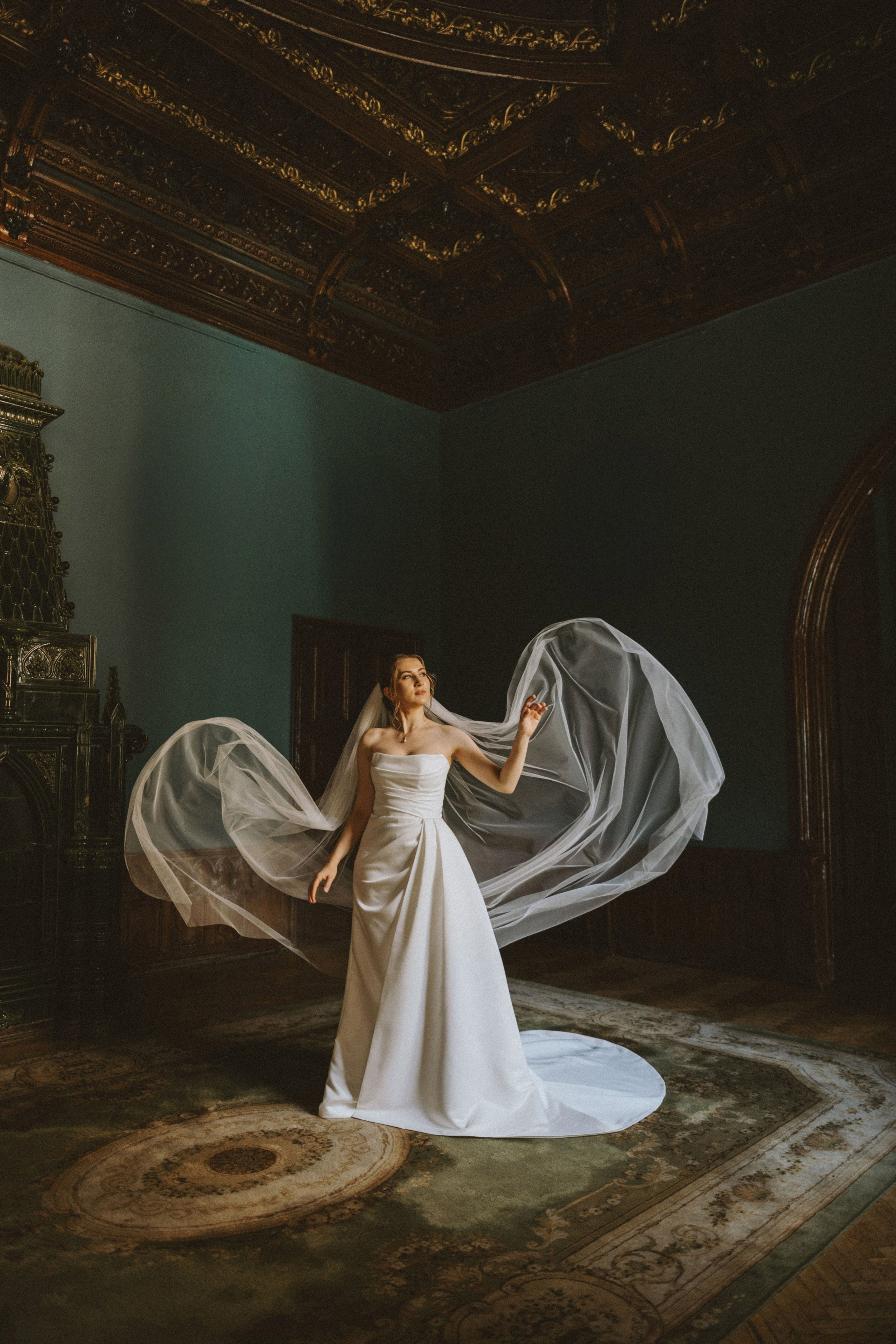 “Ritratto nuziale in un elegante ambiente interno, con la sposa in un fluente abito da sposa bianco e velo. Il velo viene drammaticamente catturato dall'aria mentre lei posa con grazia, circondata da soffitti dorati e ornati e da un ambiente lussuoso”.