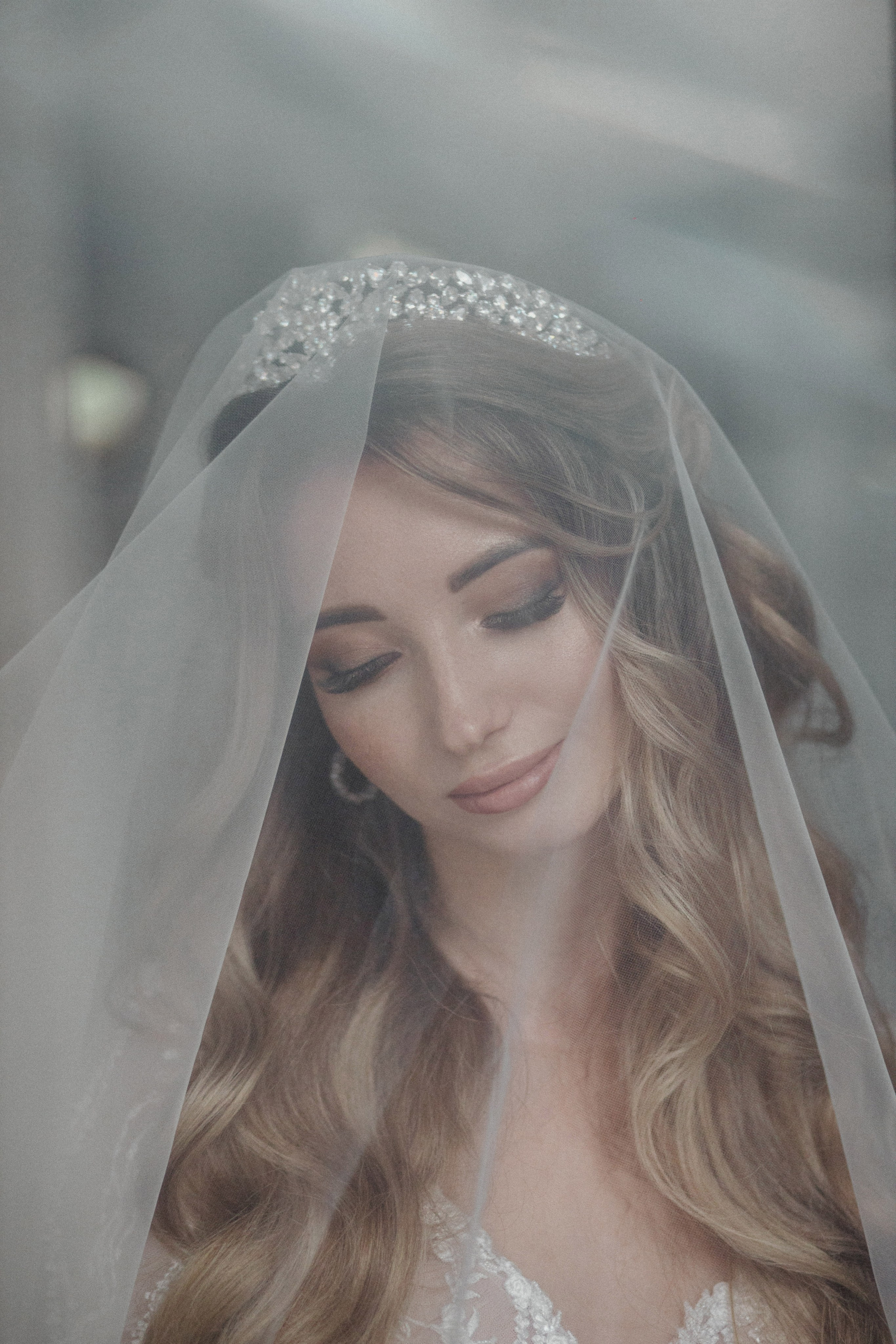 “Un ritratto ravvicinato di una sposa con un trucco morbido e naturale, che indossa un delicato velo da sposa ornato di perline scintillanti. Gli occhi sono dolcemente chiusi e i lunghi capelli ondulati le ricadono sulle spalle. Ha un'espressione serena e tranquilla, che crea un'atmosfera romantica ed elegante”.