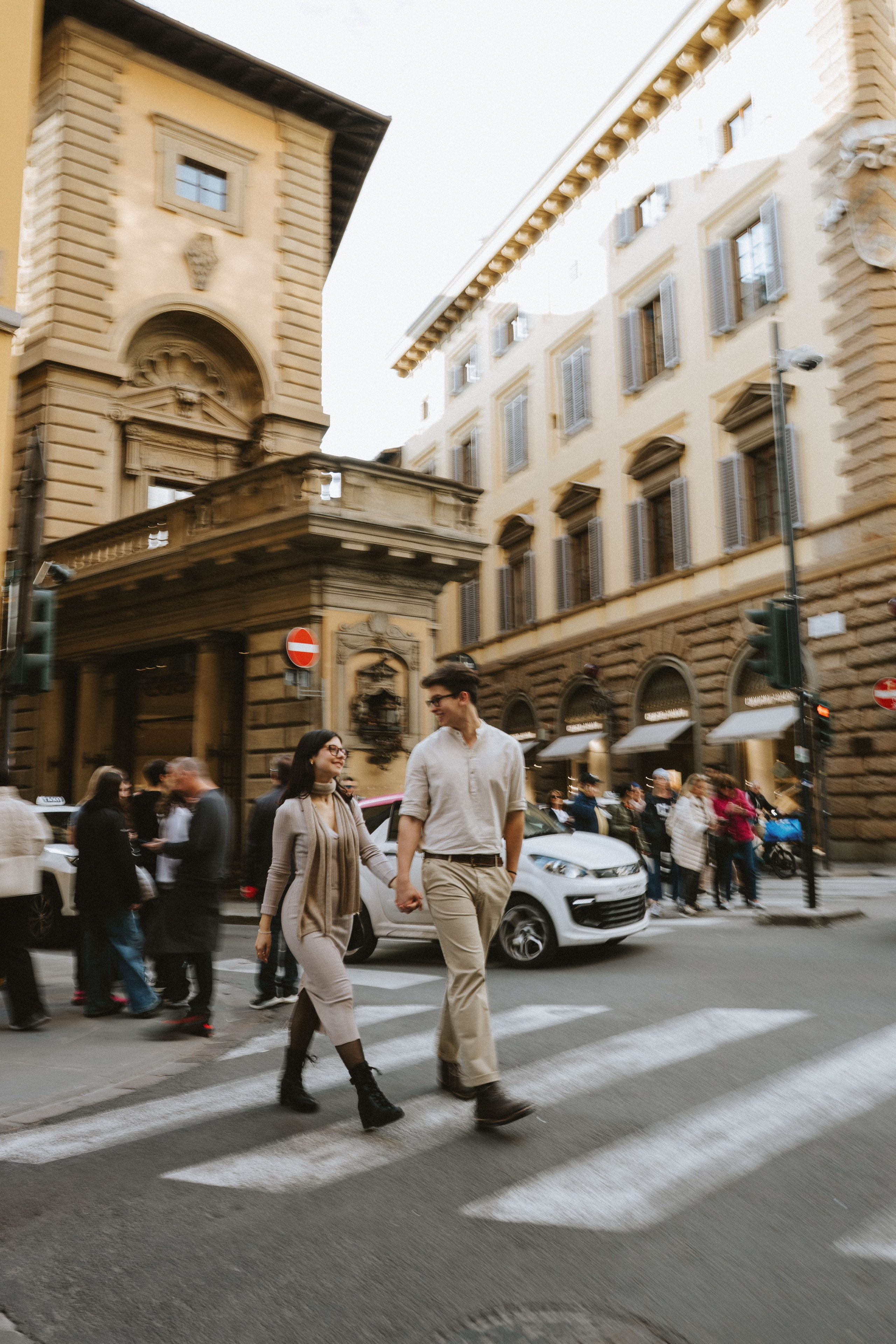 “Una coppia che cammina mano nella mano per strada a Firenze, circondata dalla vita frenetica della città”.