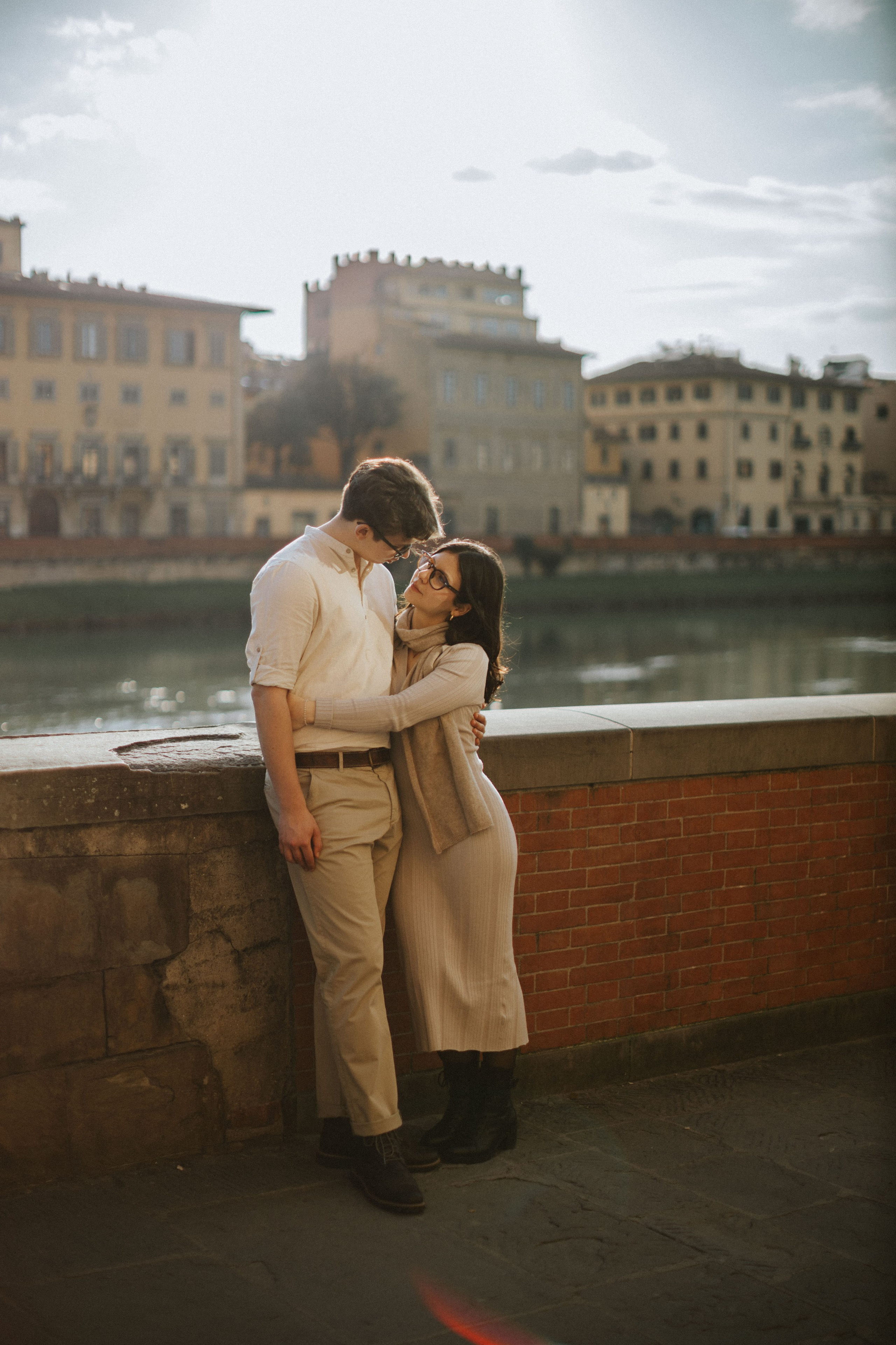 “Una coppia che condivide un momento di gioia in riva al fiume a Firenze, godendosi insieme il tramonto”.