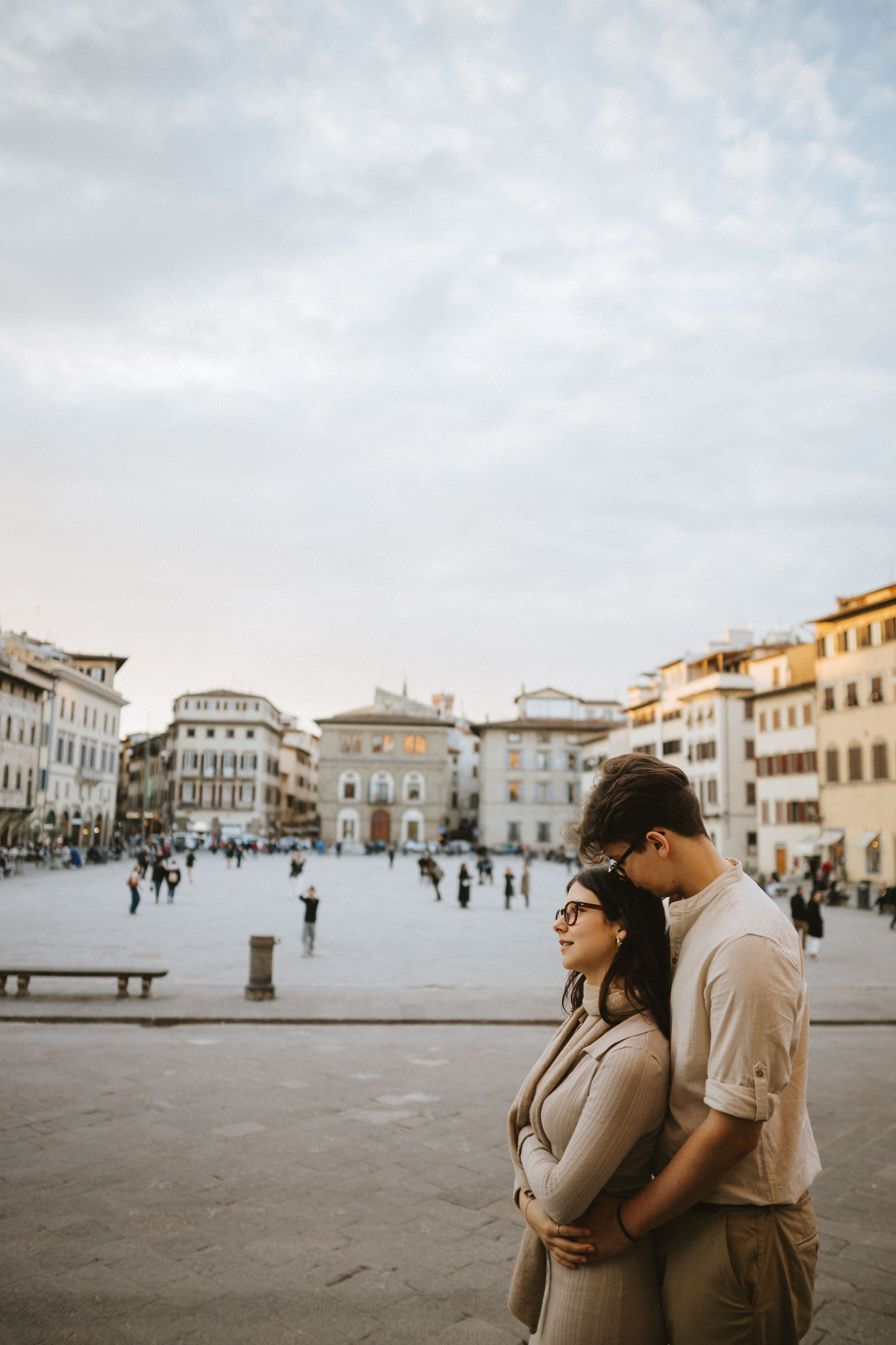 “Una coppia abbracciata, con una persona che appoggia delicatamente la testa sull'altra in una piazza panoramica”.