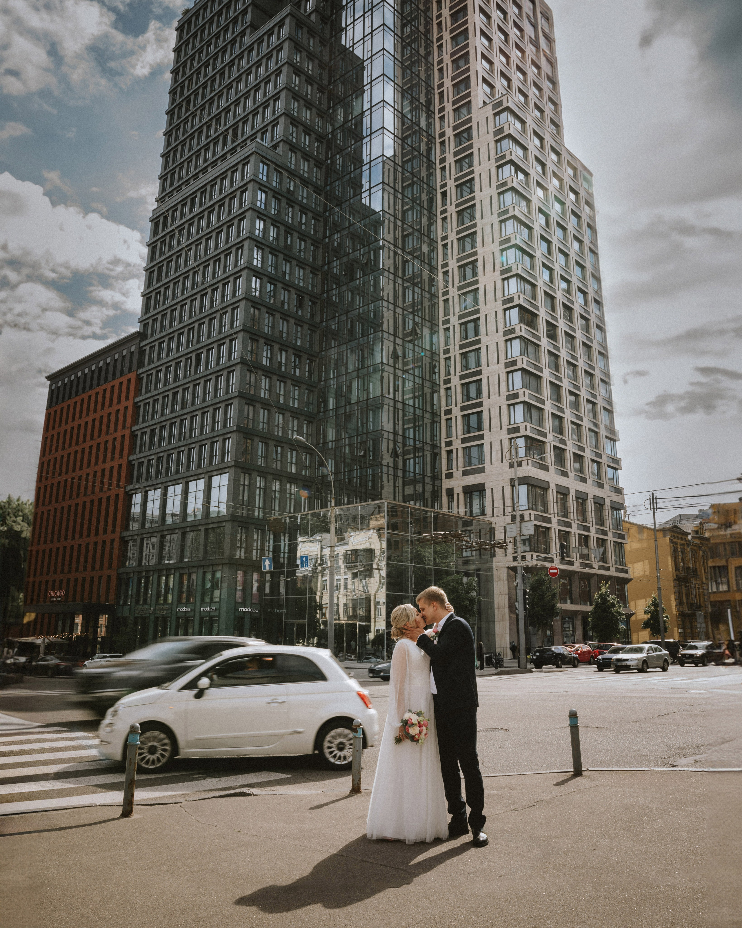 “The bride and groom exchange a tender look against the backdrop of a modern cityscape, a wedding in Milan or Turin.”