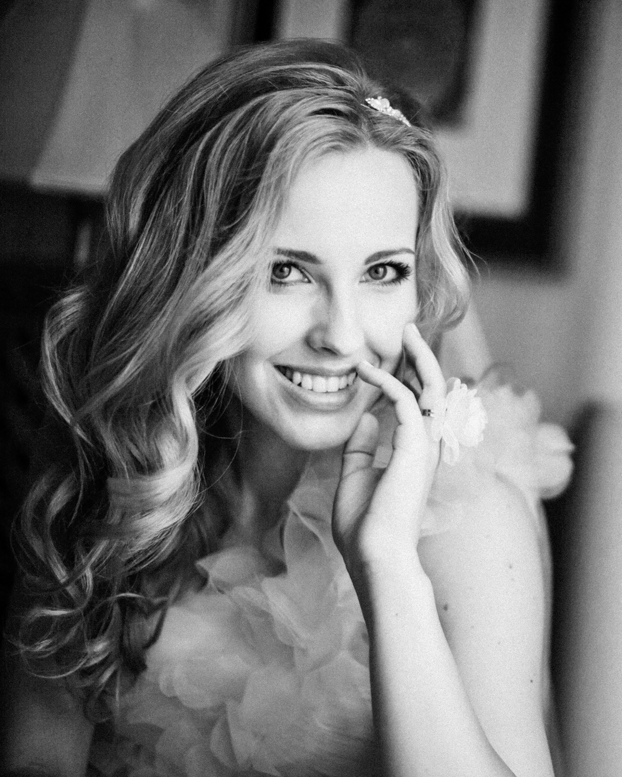 “Black and white portrait of the bride smiling, with soft makeup and a hair accessory.”