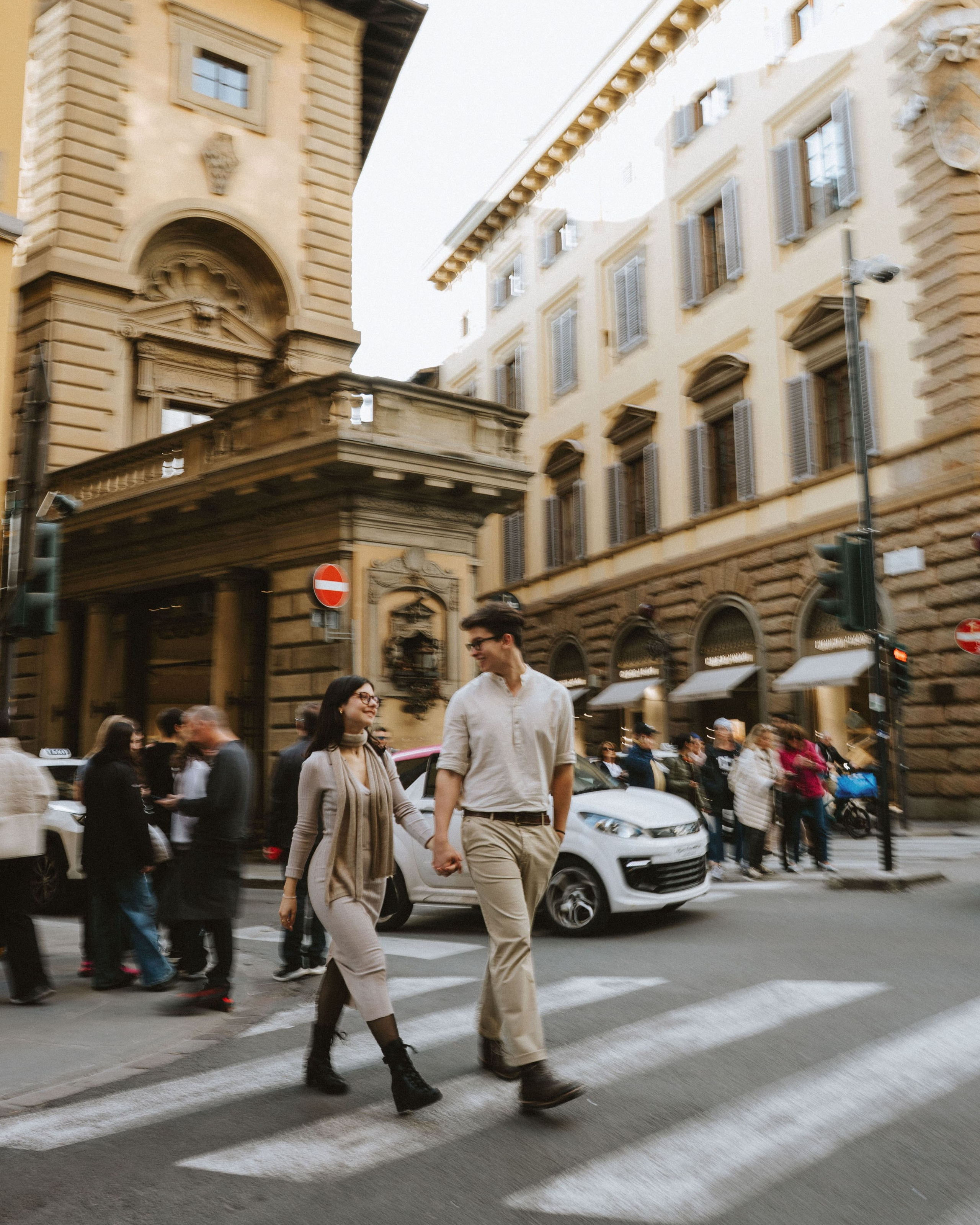 “A couple walking down the street in a historic Renaissance district, holding hands.”