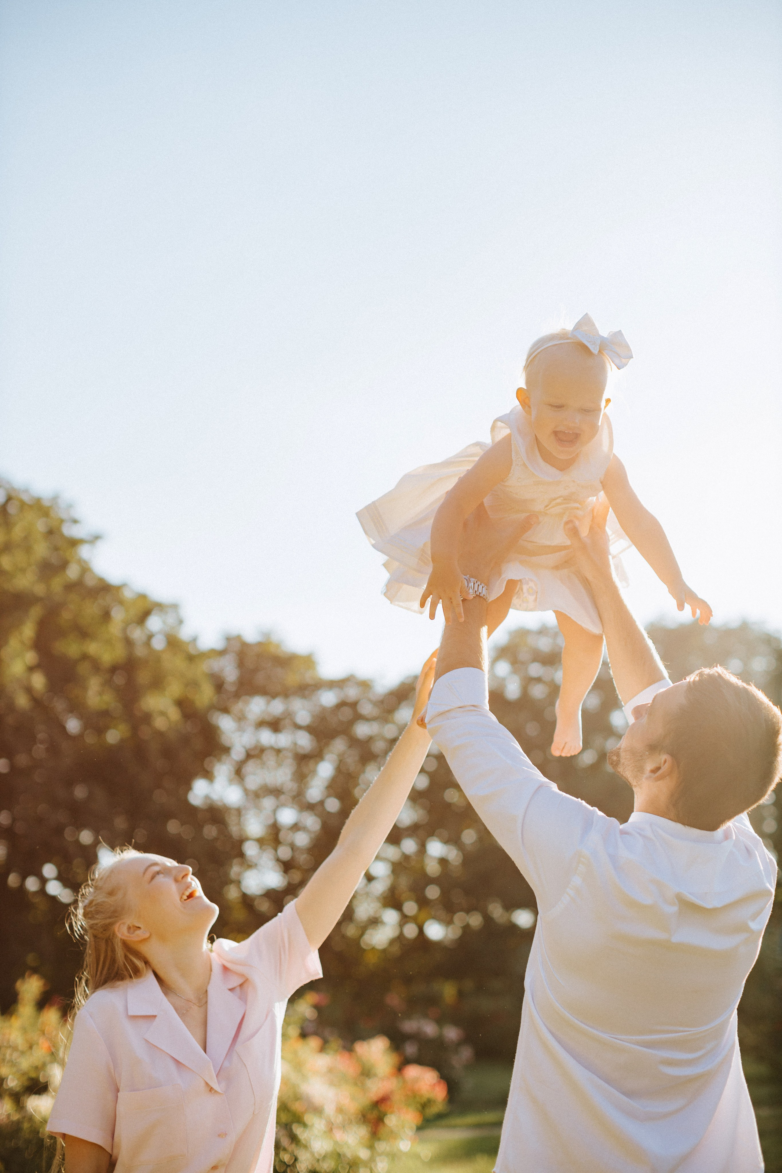 “Un momento gioioso di una famiglia che gioca insieme alla luce del sole. Il padre solleva in aria la figlia piccola, mentre la madre sorride e allunga la mano. La figlia indossa un vestito bianco e un fiocco e si gode il momento”.