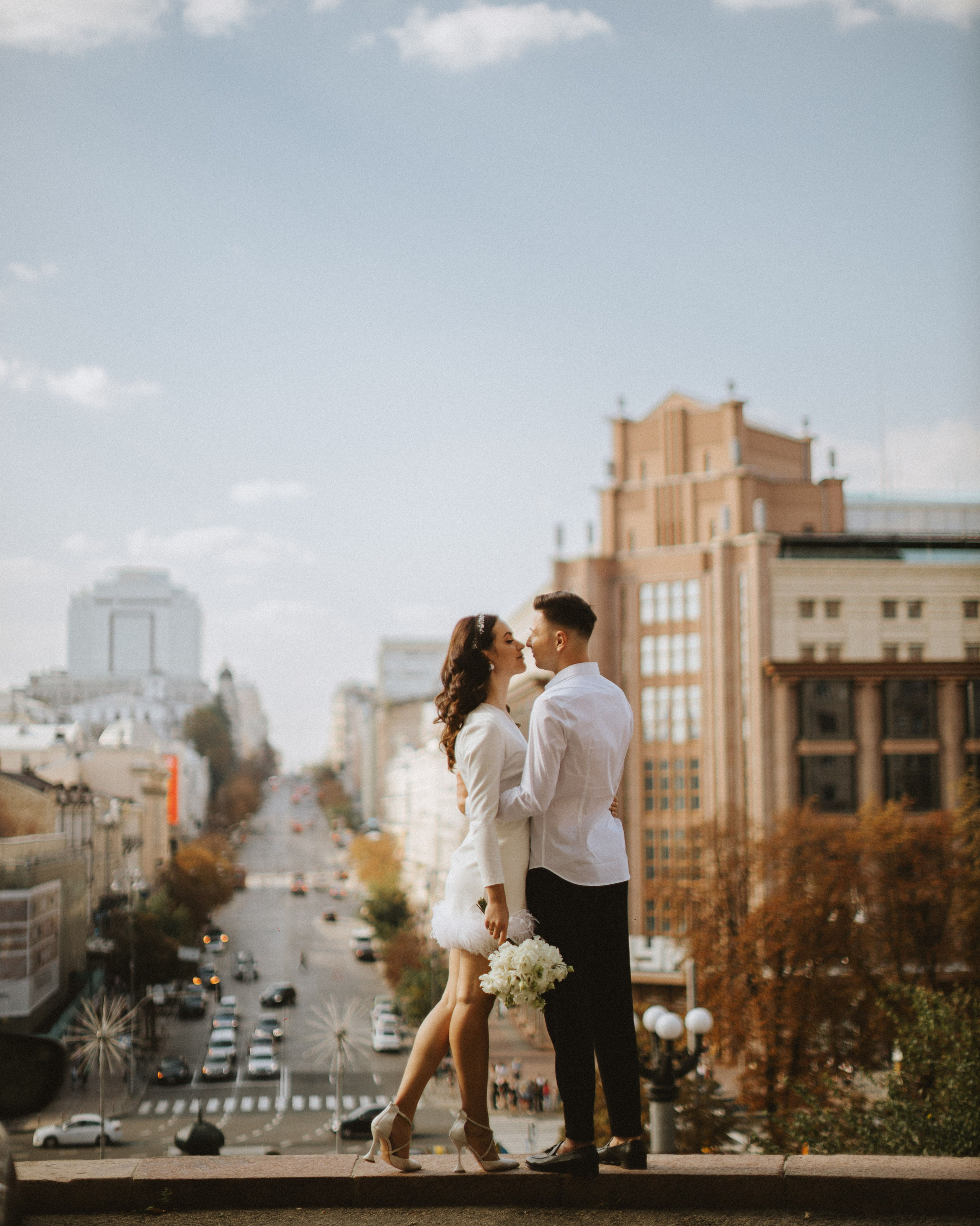 “The bride and groom share a kiss against the backdrop of the cityscape, the bride holding a bouquet.”