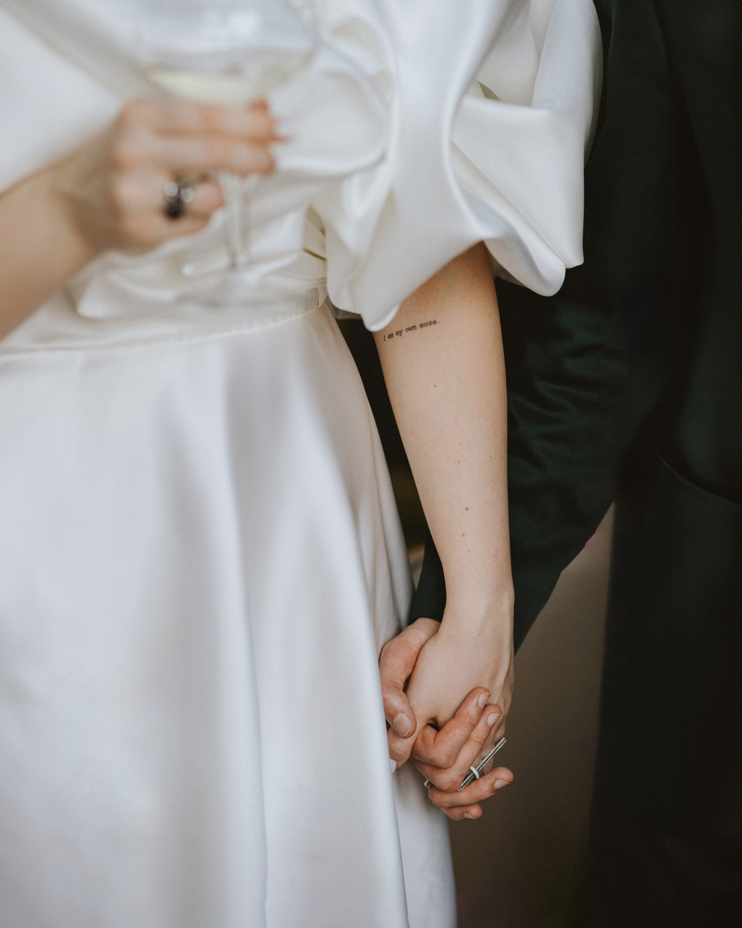 “Fotografo di matrimonio che cattura un momento di intimità tra gli sposi che si tengono per mano. La sposa, in uno splendido abito da sposa, ha un tatuaggio sul braccio con la scritta 'Sono la mia musa'. Uno scatto bello e significativo per un matrimonio in Toscana, Italia”.