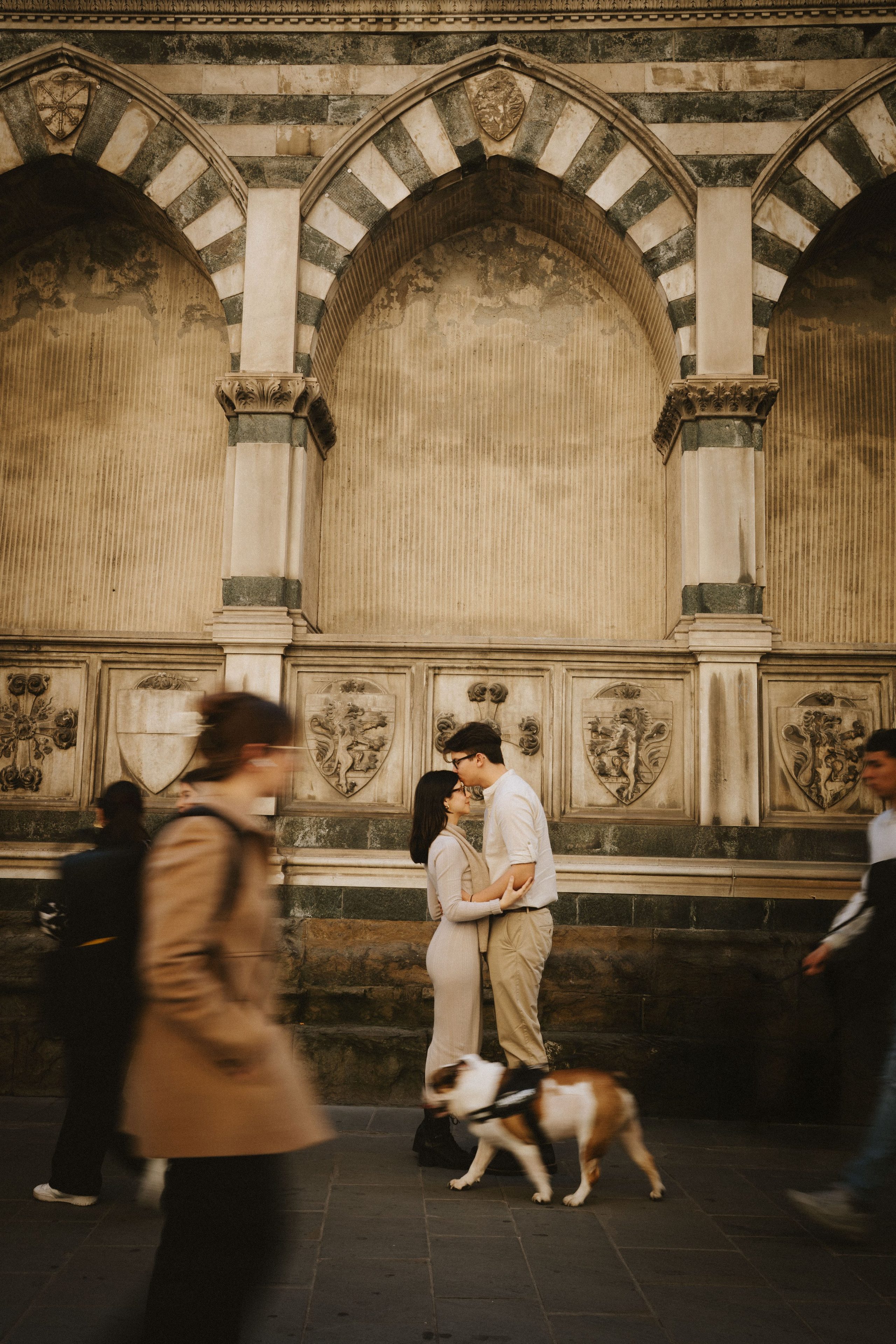 “Una coppia che si scambia un bacio a Firenze, con una strada animata e un cane che passeggia”.