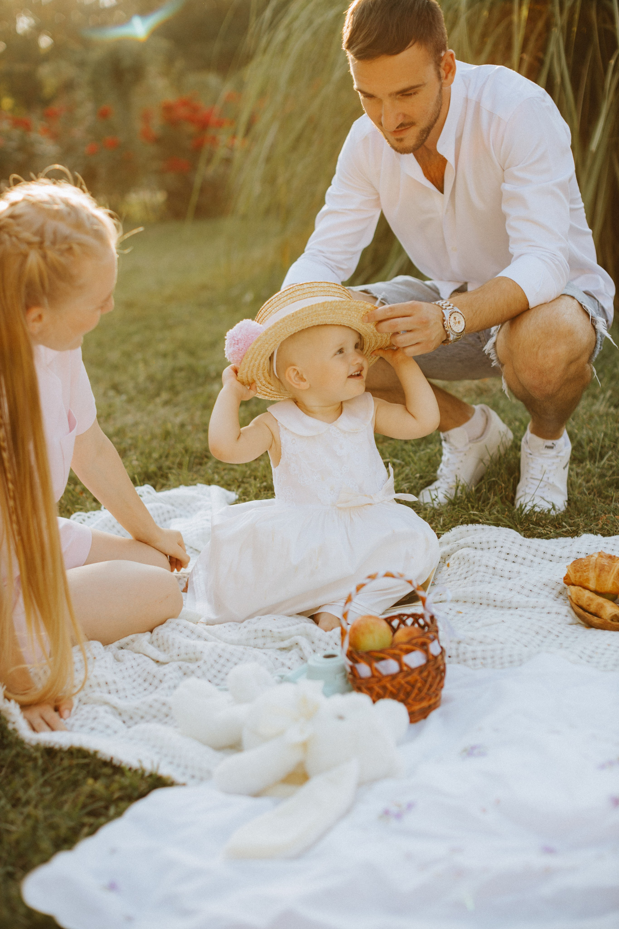 “Una famiglia che si gode un picnic nel parco, con il padre che mette un cappello al suo bambino sorridente. La madre siede vicino e la scena è piena di coperte, peluche e cibo, il tutto illuminato dalla luce soffusa del sole”.