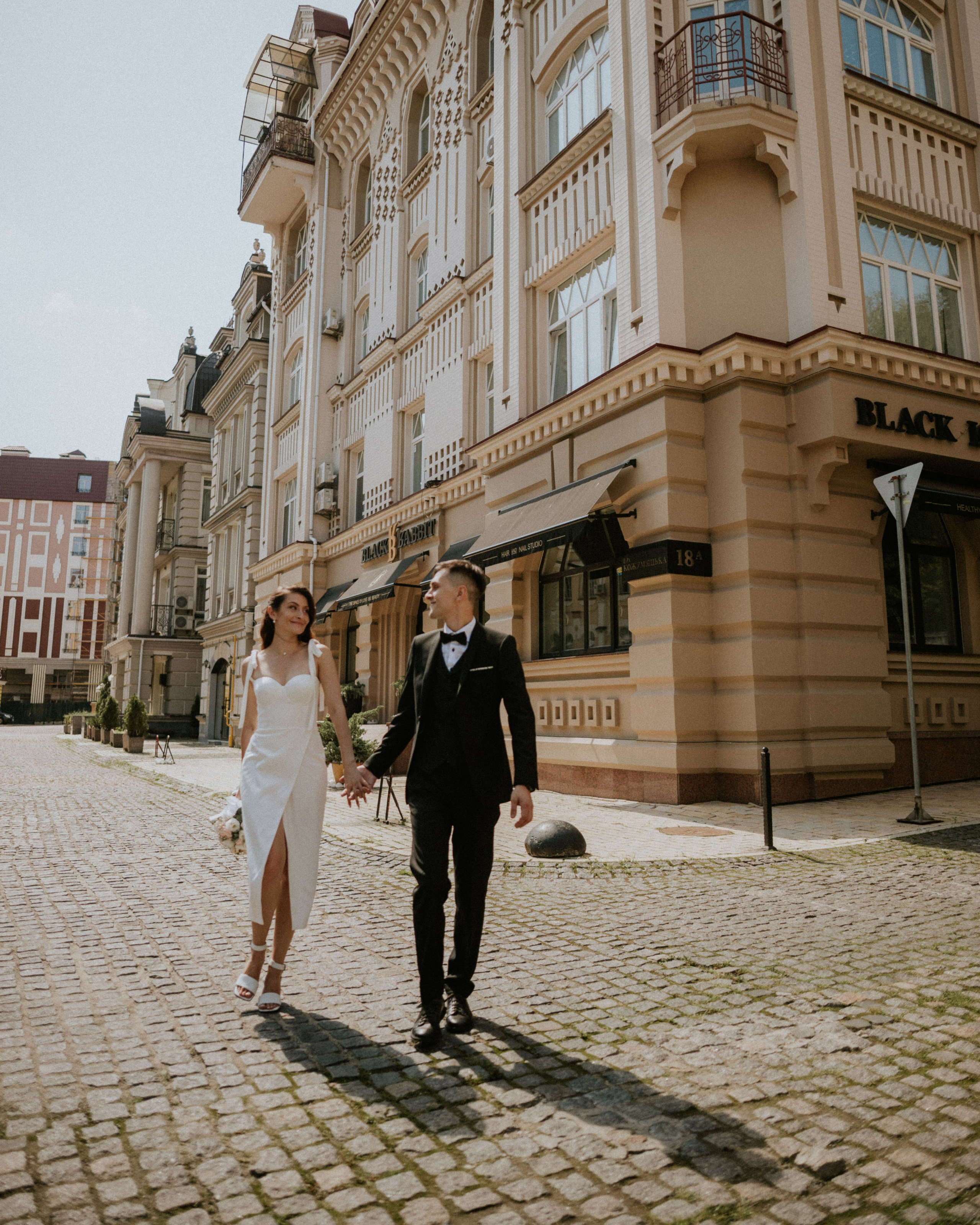 “The bride in a stylish dress and the groom in a suit walk along the street, surrounded by architecture, a wedding in Milan or Rome.”