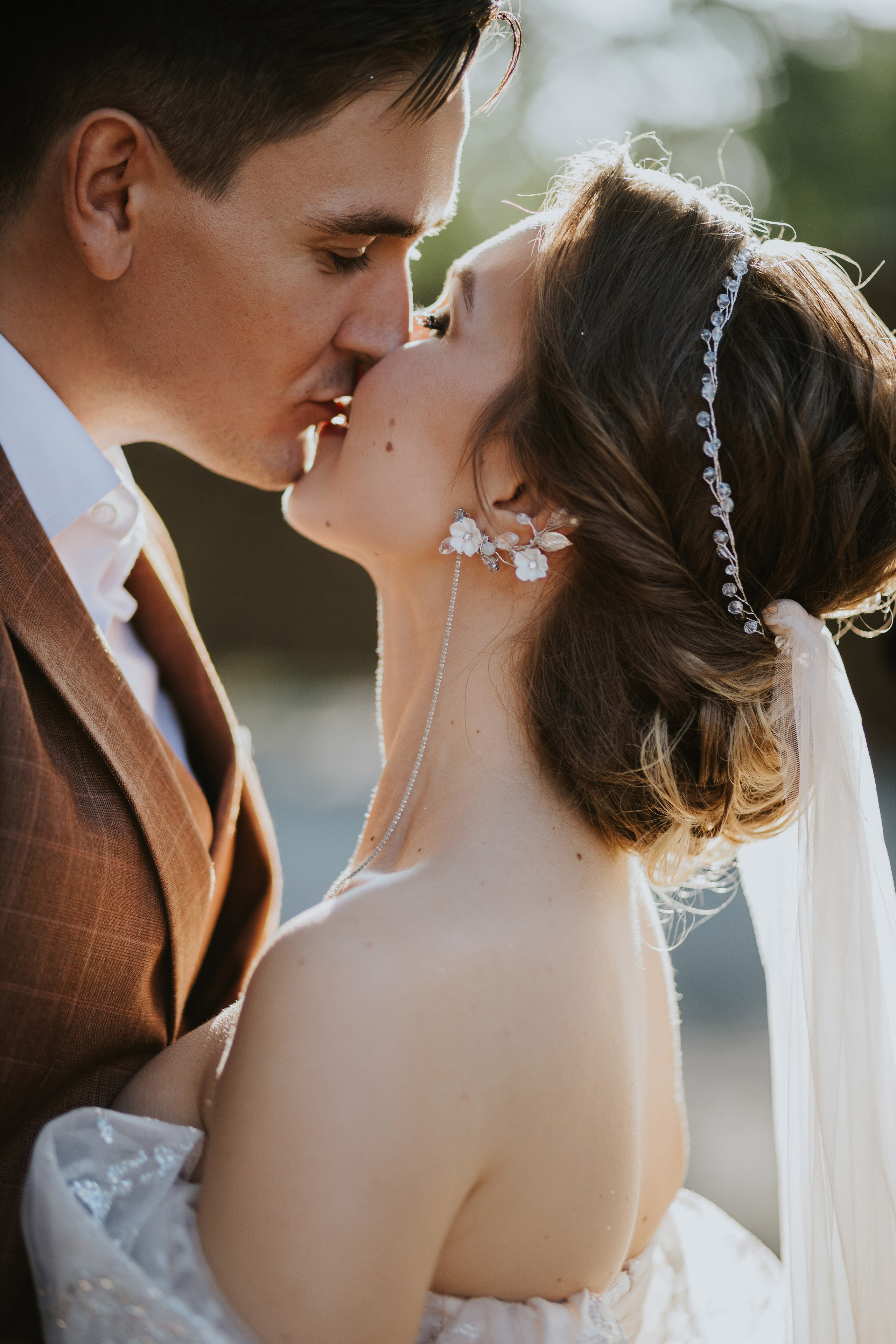 “Primo piano di una coppia che si bacia durante il servizio fotografico di matrimonio. La sposa indossa eleganti orecchini floreali e un delicato parrucchino, mentre il viso dello sposo è delicatamente premuto contro il suo”.
