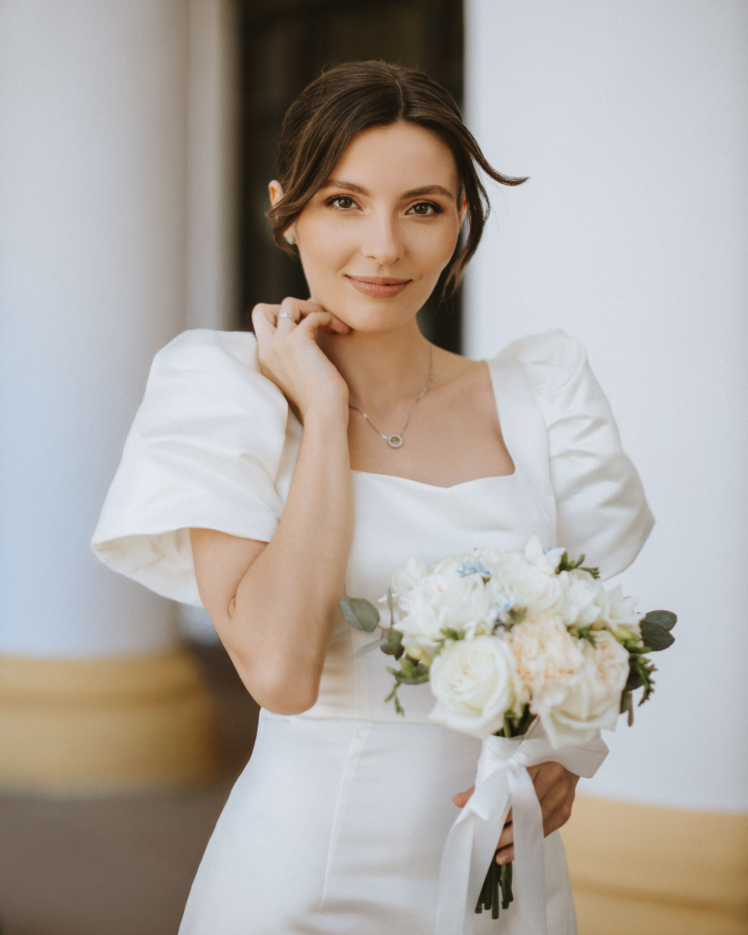 “The bride in a white dress holding a bouquet of white flowers, smiling and standing against the backdrop of architecture in Italy, possibly in Rome or Florence.”