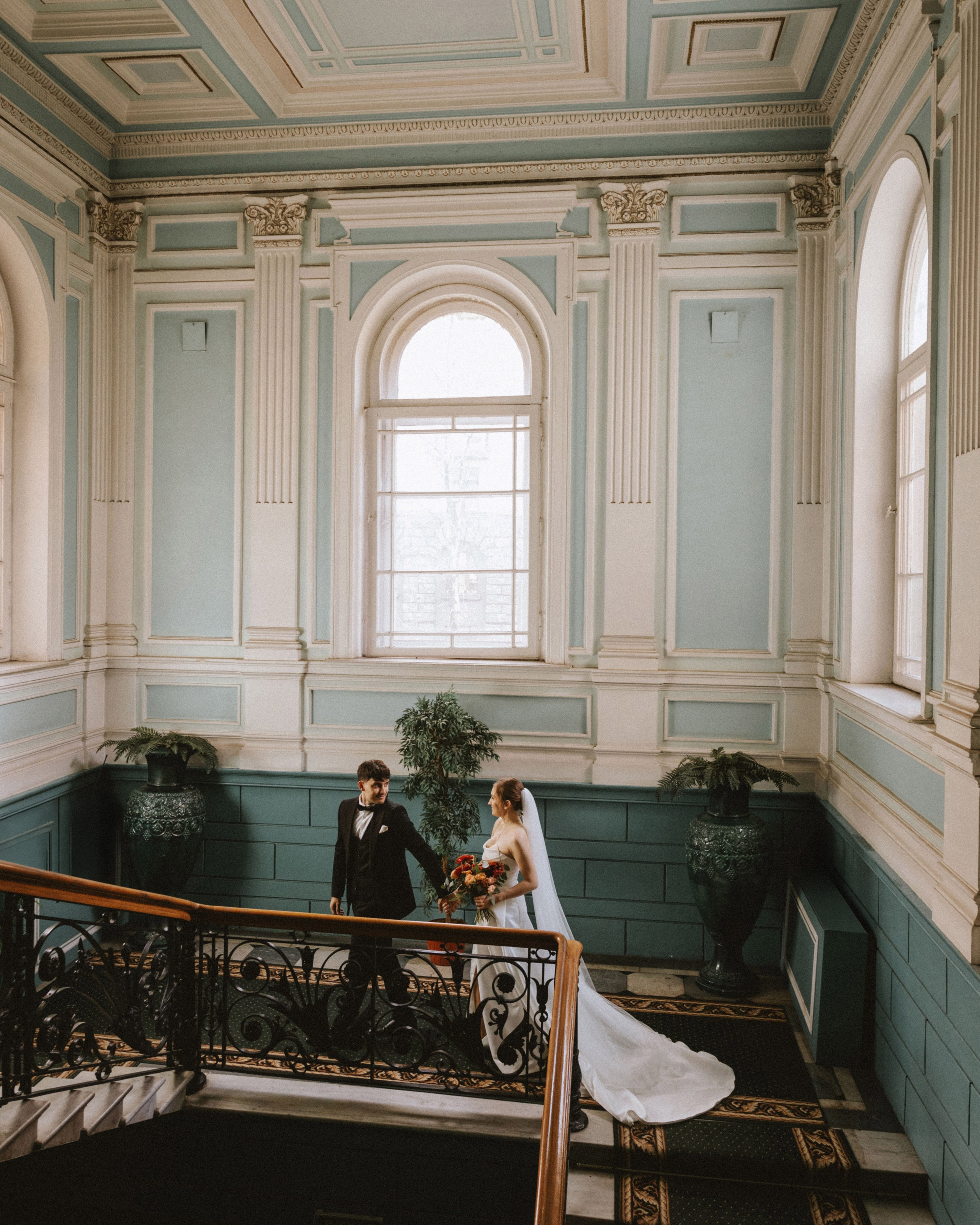 “The bride and groom on the staircase in a historic interior, with the bride holding a floral bouquet, a wedding in Venice or Sicily.”