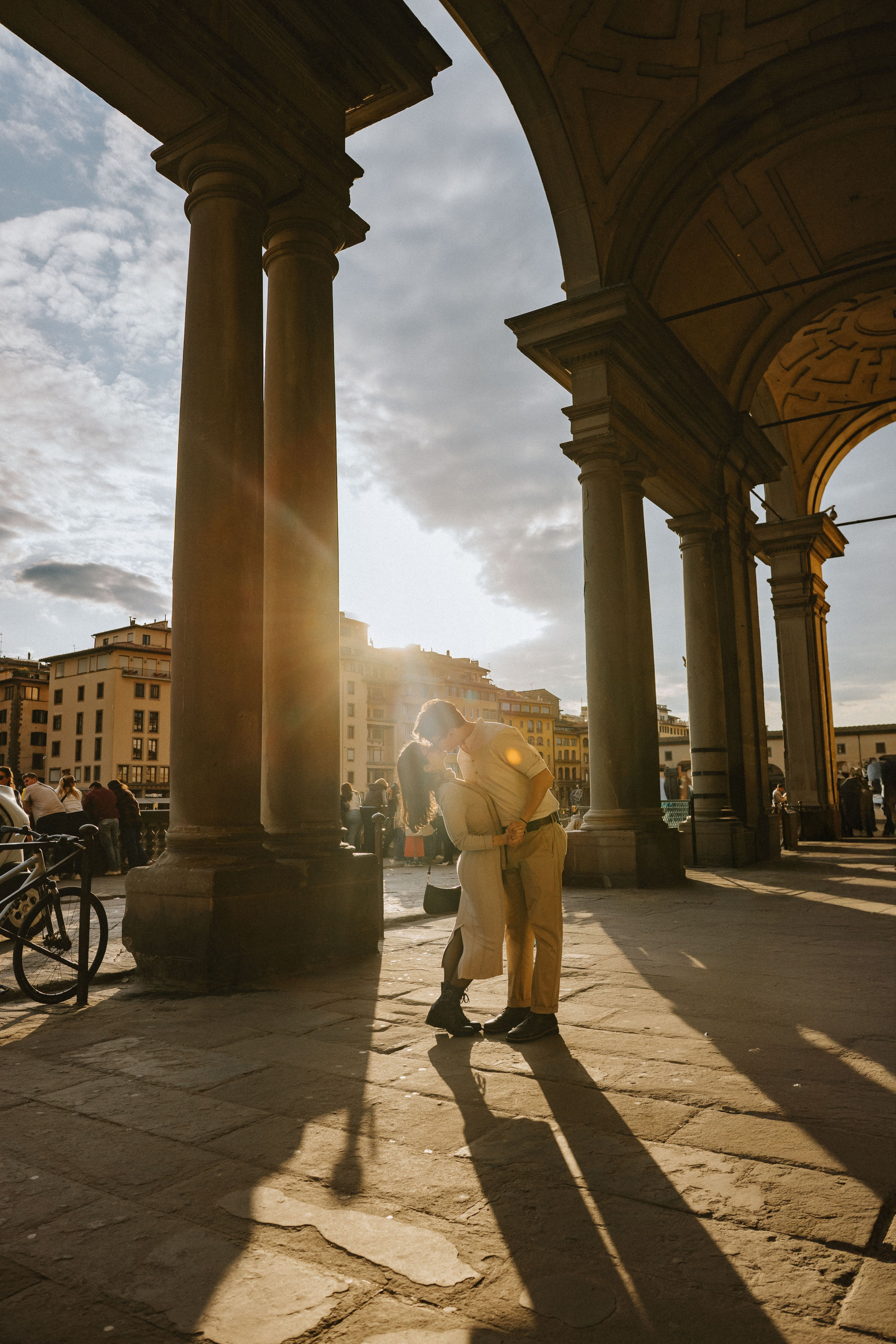 “Coppia che si scambia un bacio romantico nell'ora d'oro, incorniciata da colonne architettoniche”.