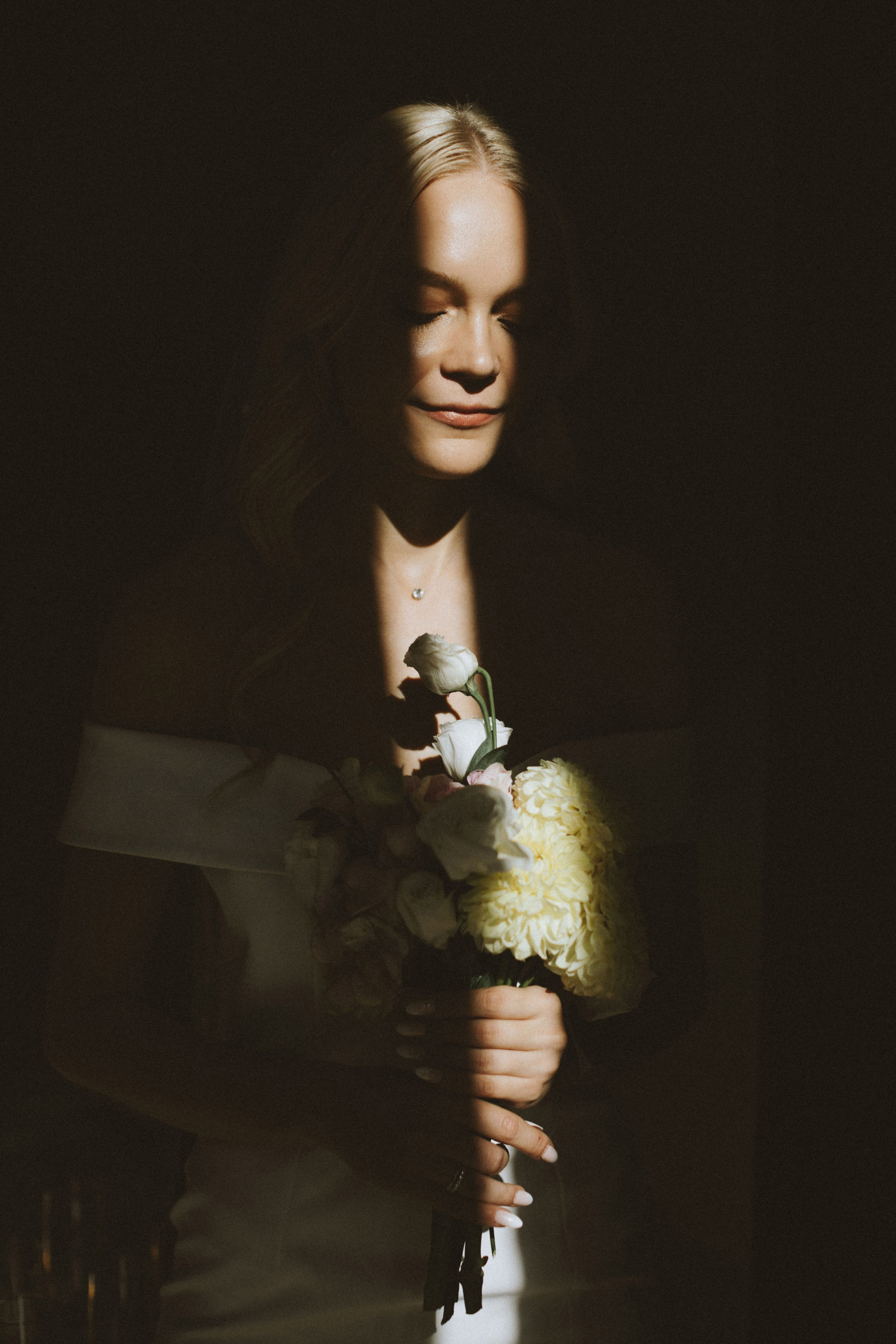 “Una sposa in piedi in una stanza poco illuminata, con la luce che proietta un'ombra drammatica sul suo viso. Tiene tra le mani un bouquet di fiori, dai colori tenui e chiari. I suoi occhi sono chiusi e la sua espressione è calma e serena, che trasuda un momento di pacifica contemplazione”.