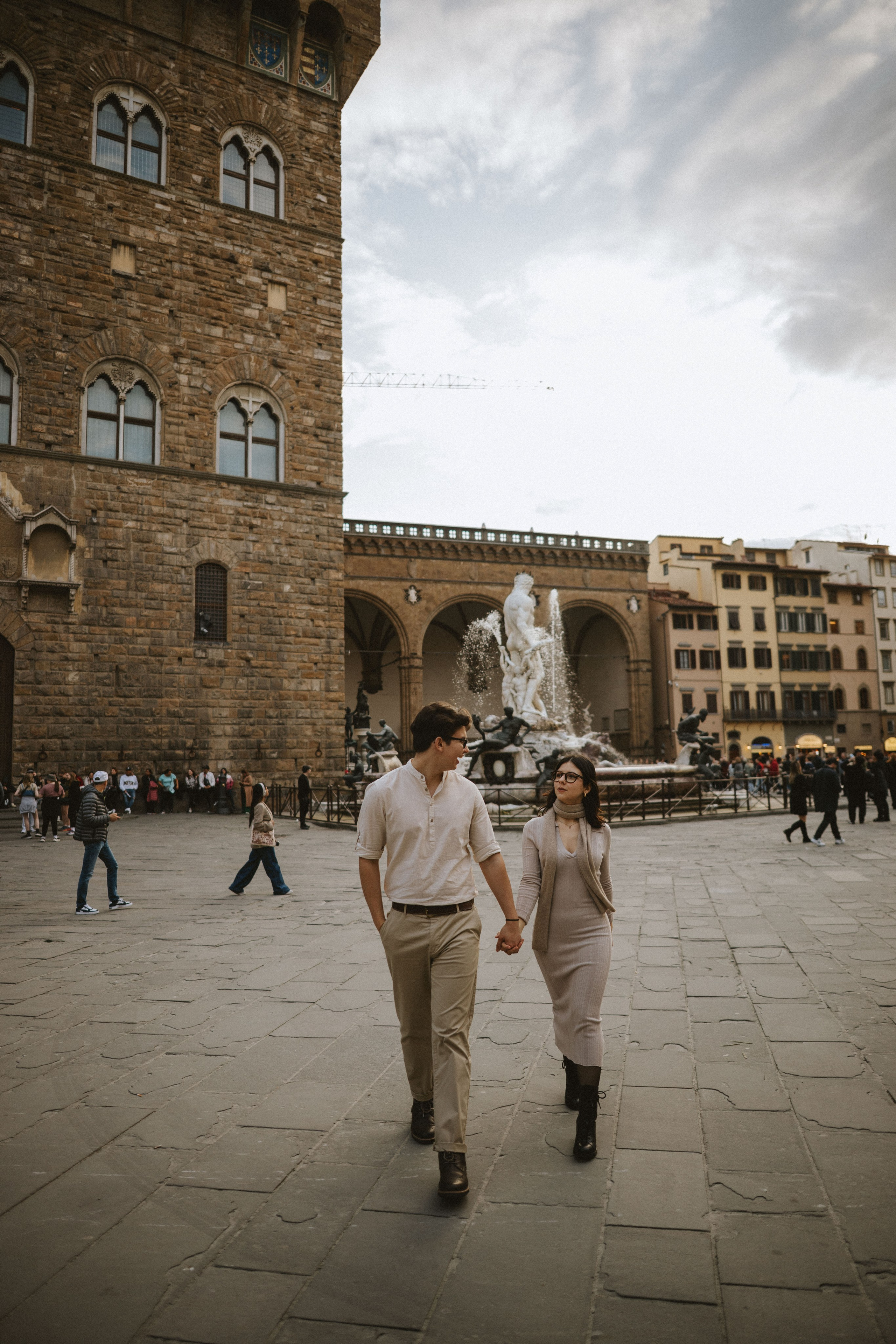“Coppia che passeggia mano nella mano a Firenze, con una bella fontana ed edifici storici sullo sfondo”.