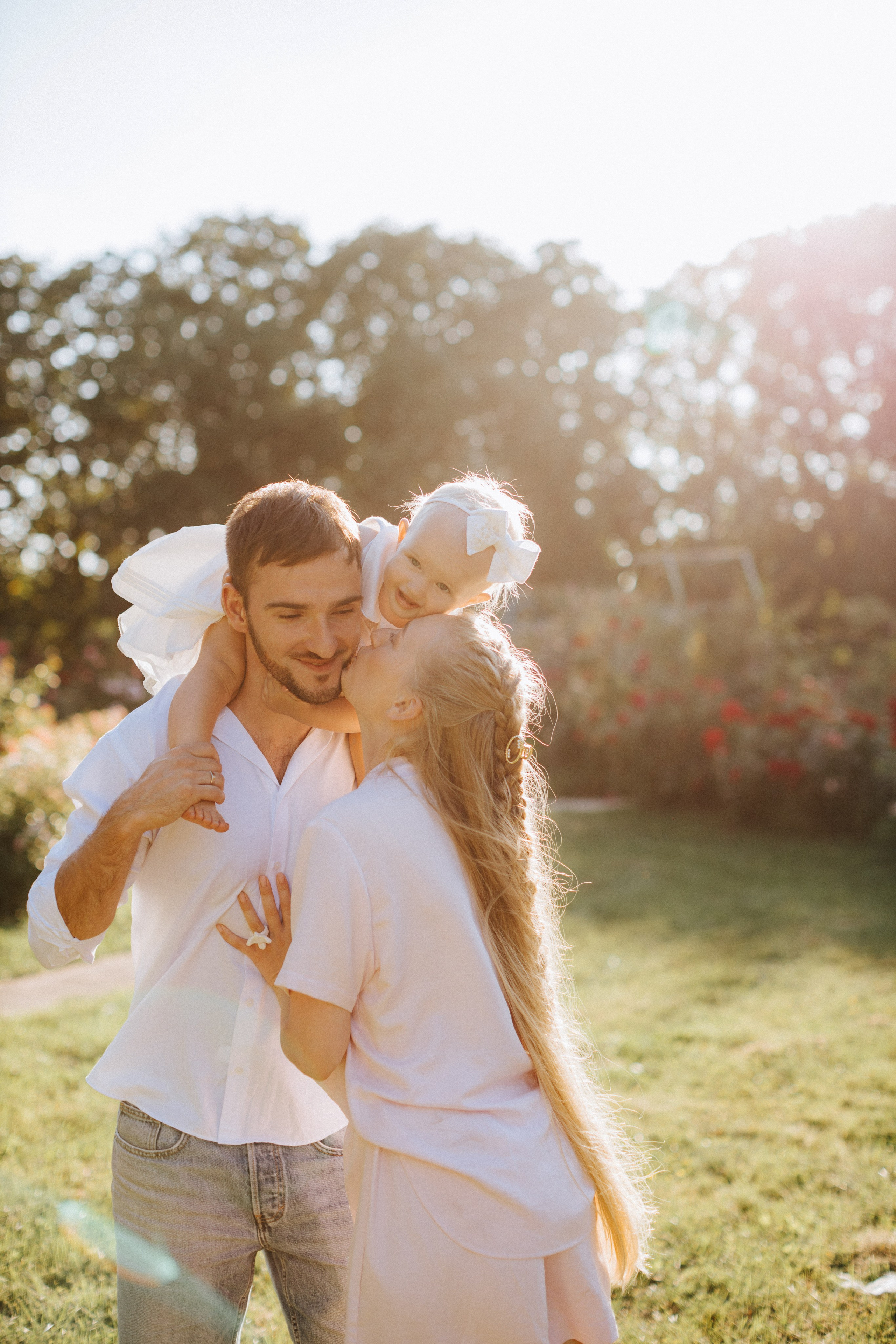 “Una gioiosa famiglia di tre persone si gode il tempo all'aria aperta. Il padre tiene la figlia sulle spalle, mentre la madre si china a baciarlo. La calda luce del sole filtra attraverso lo sfondo, creando un morbido bagliore dorato nella scena”.