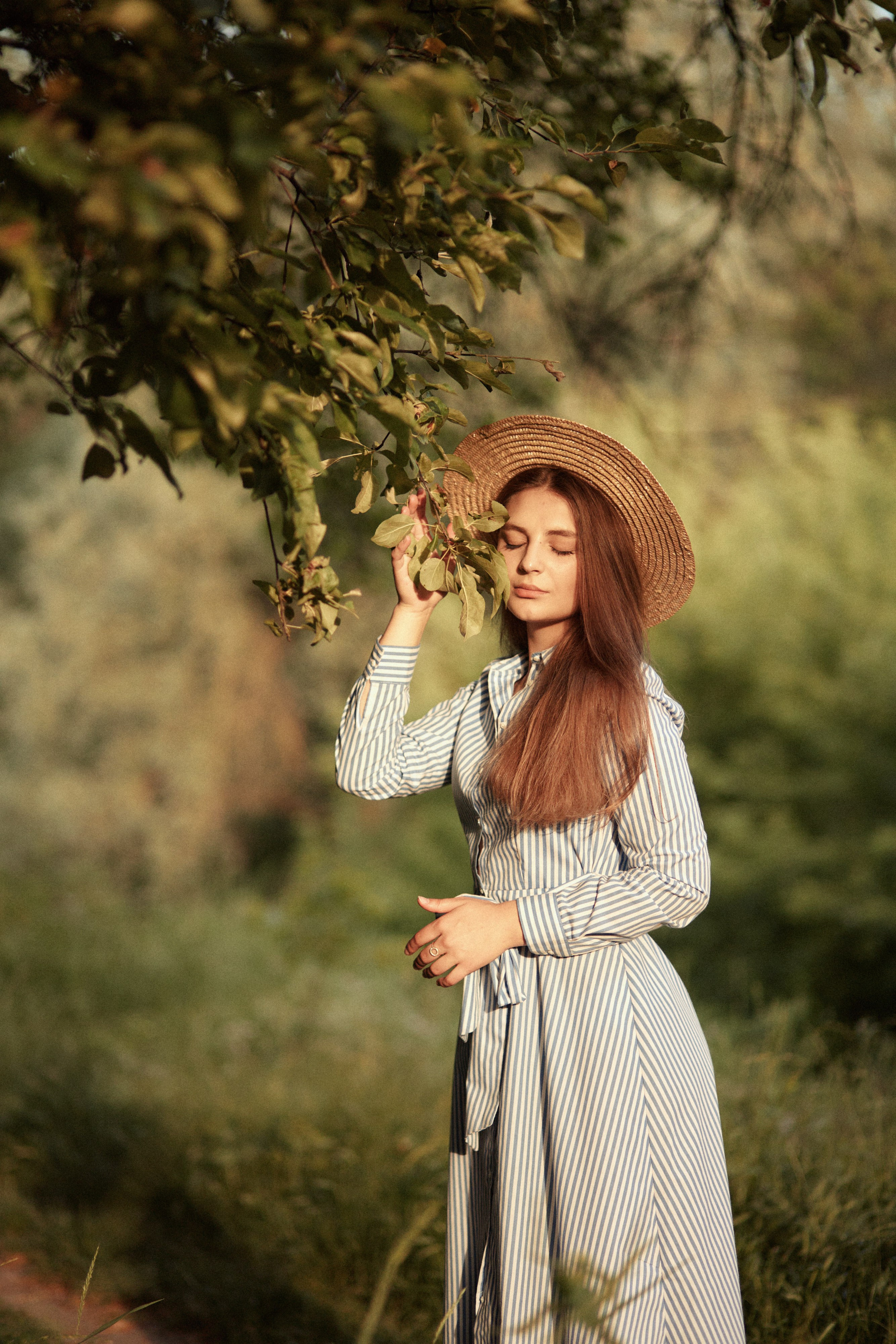 Романтичний портрет у саду — дівчина в капелюсі торкається гілки