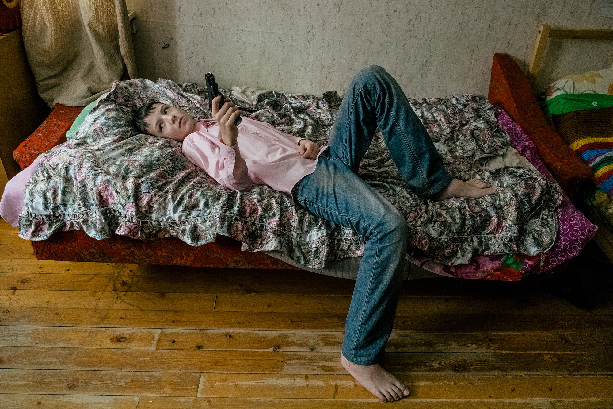 A boy with a gun is lying on the bed. Мальчик с пистолетом лежит на кровати.