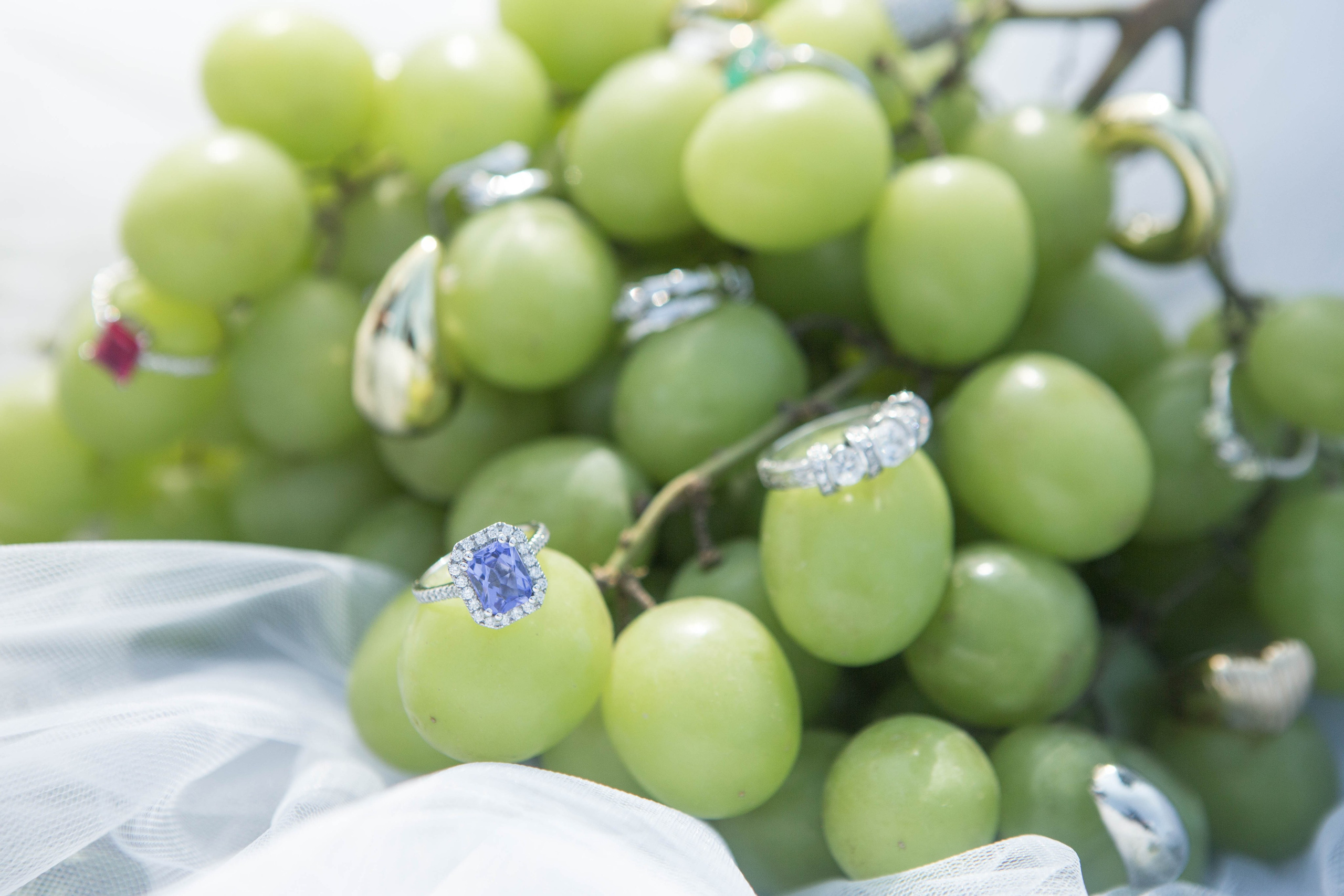Close-up of wedding rings and jewelry arranged on clusters of grapes in a creative still-life setup