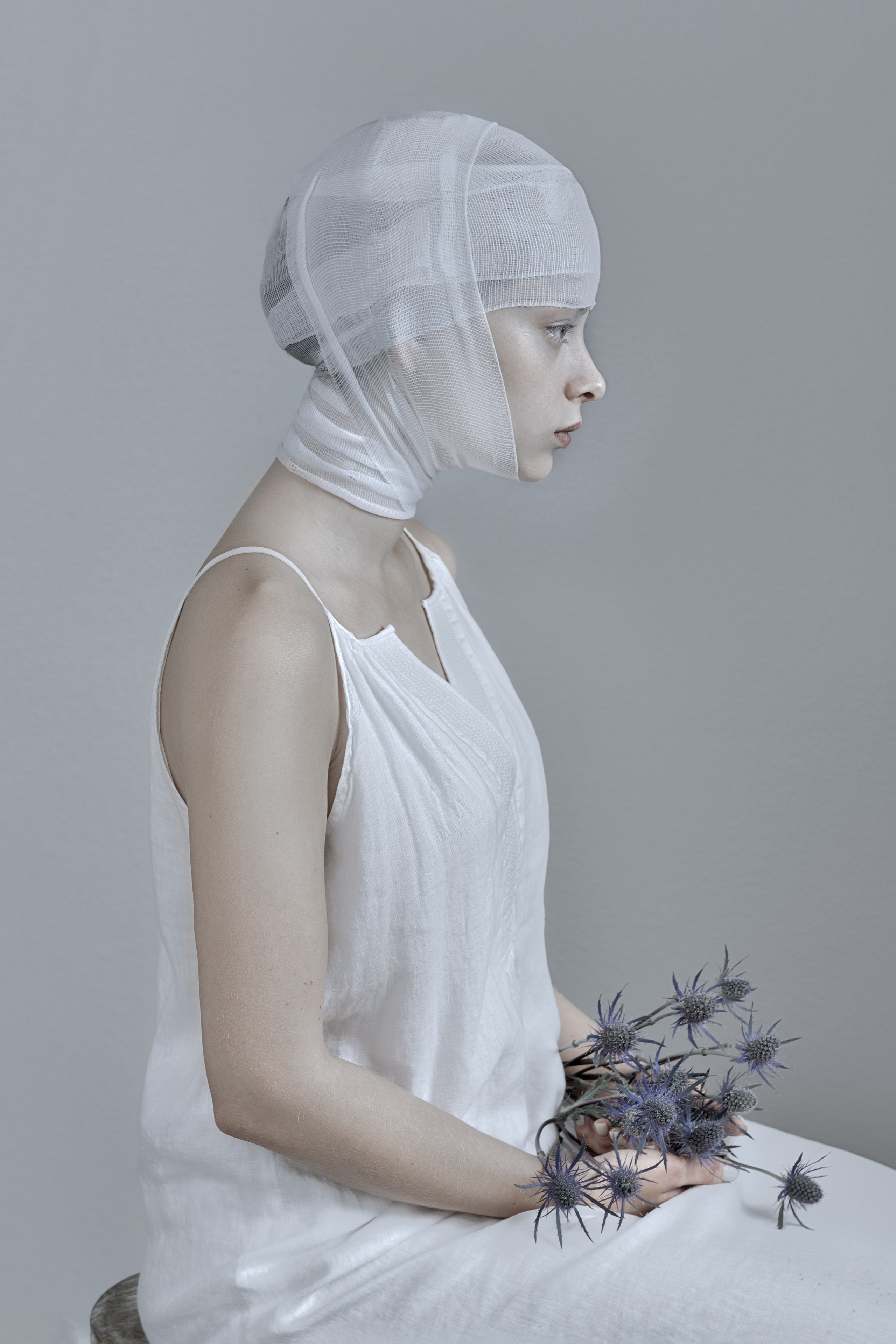 Woman in white holding thistles, portrays introspection and solitude
