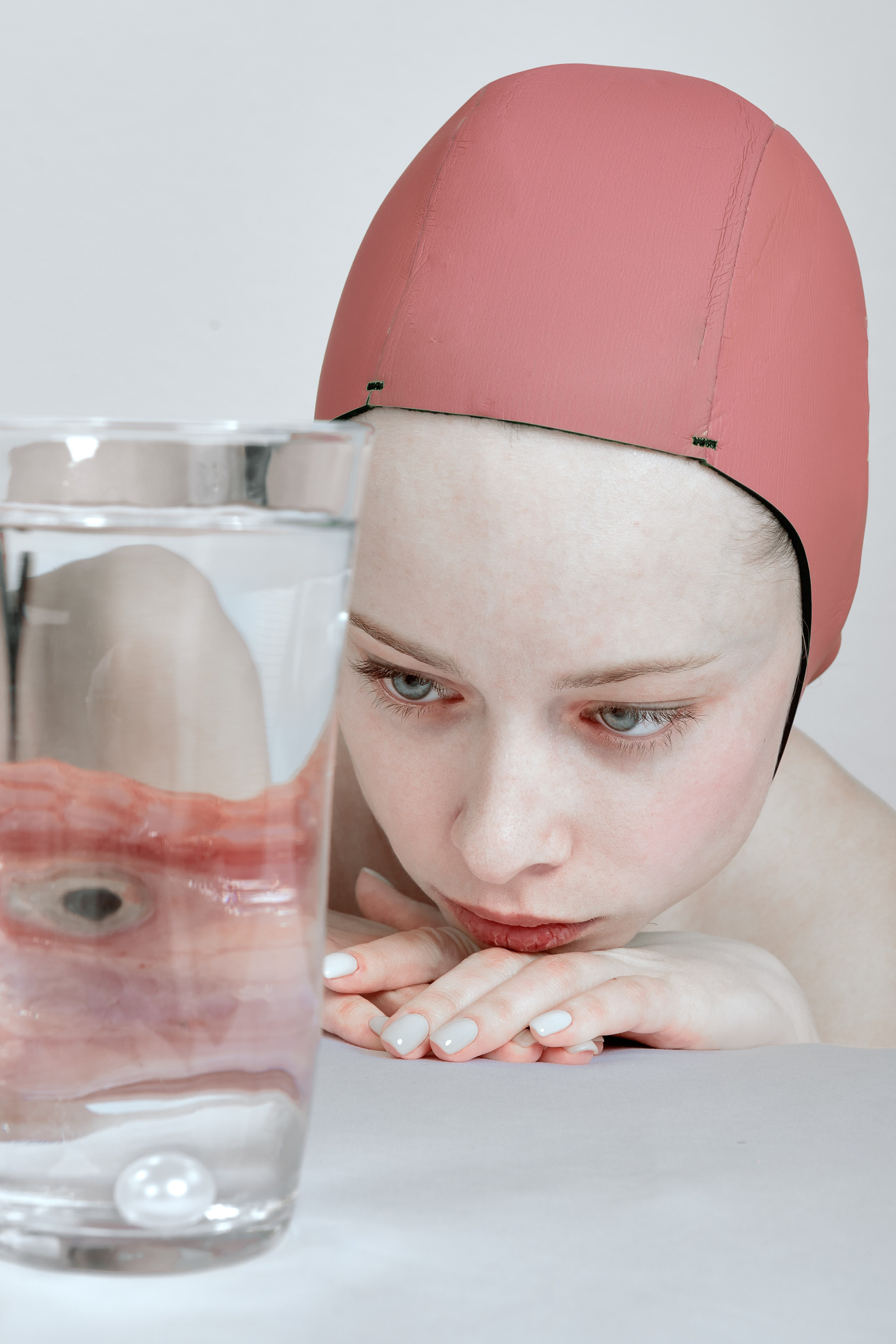 Woman observing eye in water glass, reflecting on identity and displacement