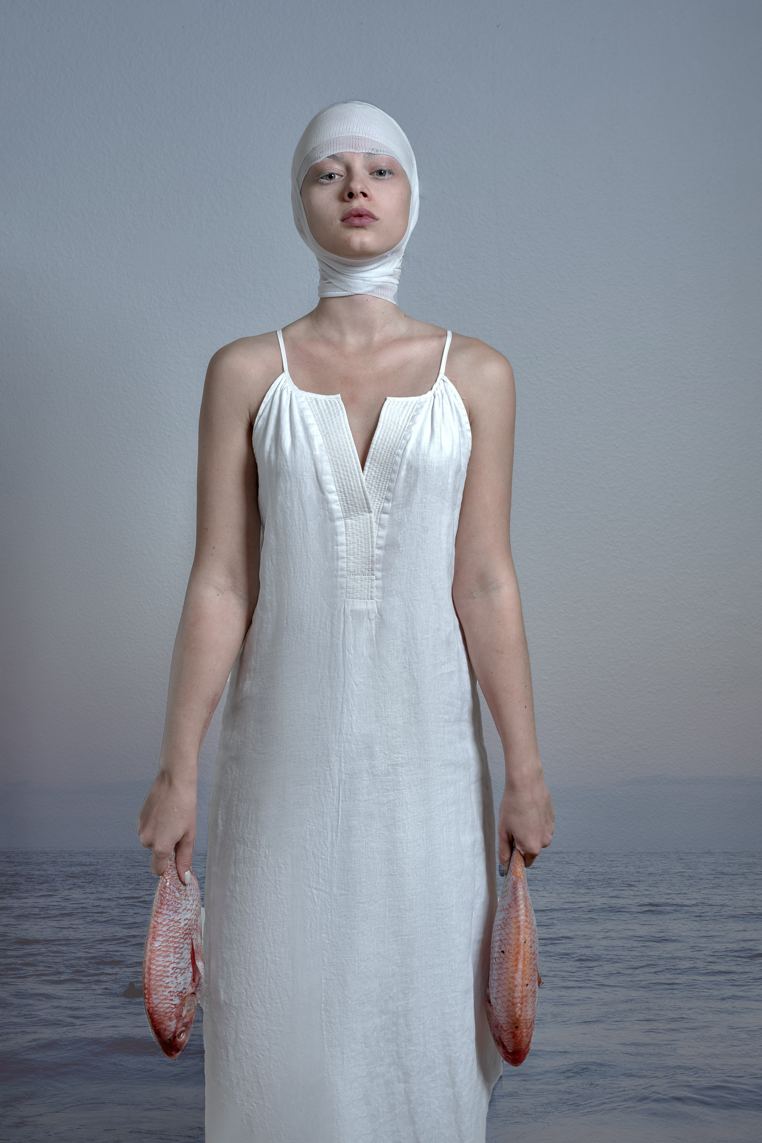 Woman in white dress and headband, holding fish, symbolizes new life challenges.