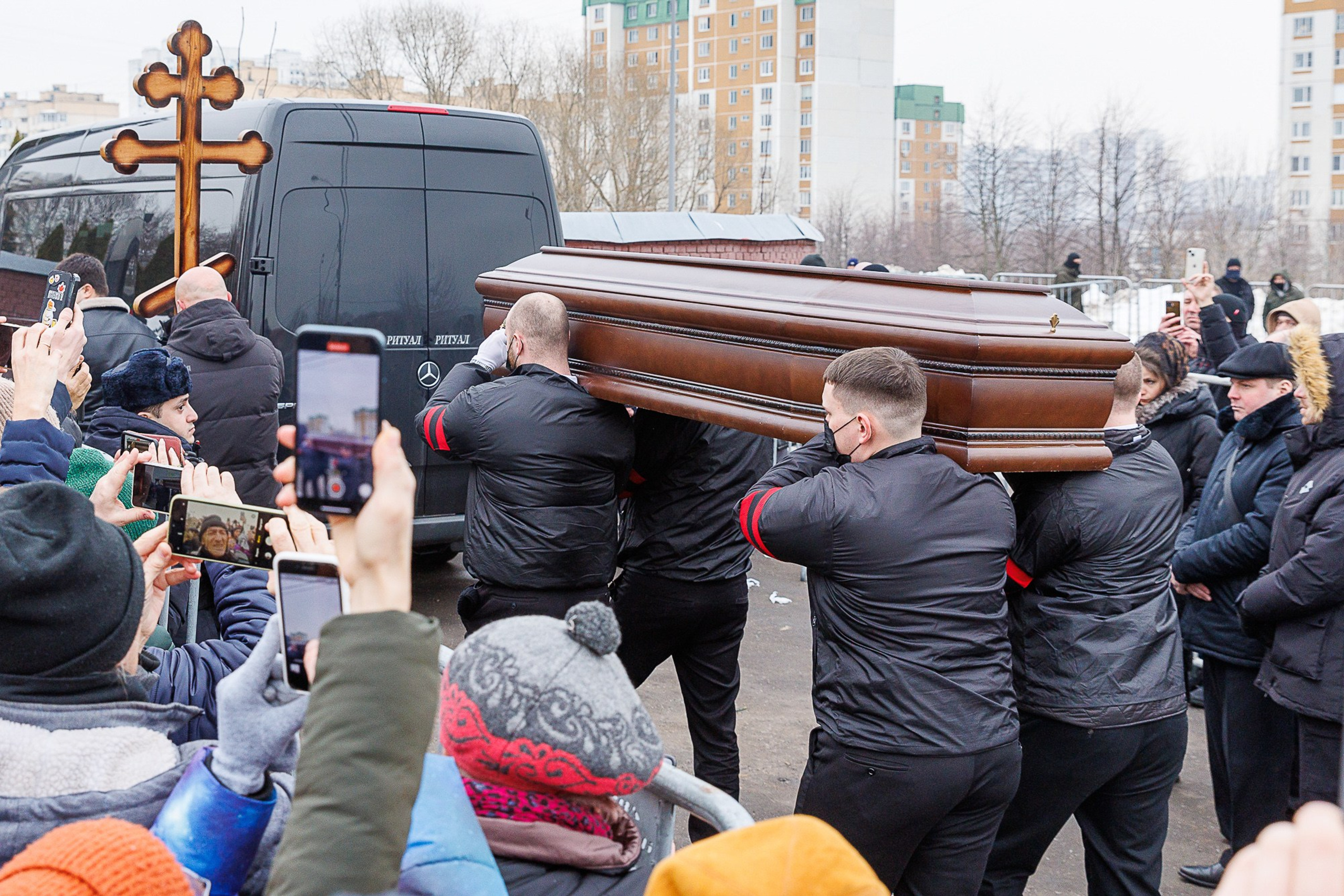 Navalny lying in coffin surrounded by flowers and priest, 2024