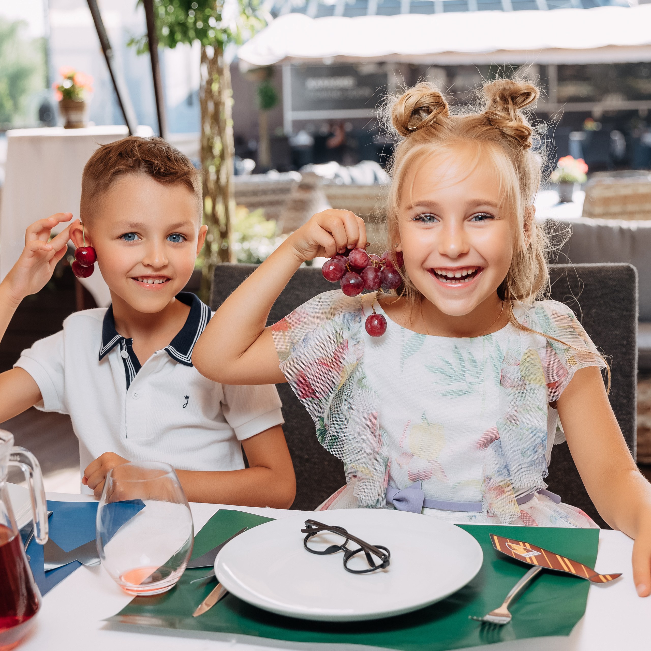 Мальчик и девочка смеются и показывают виноград на ушах.