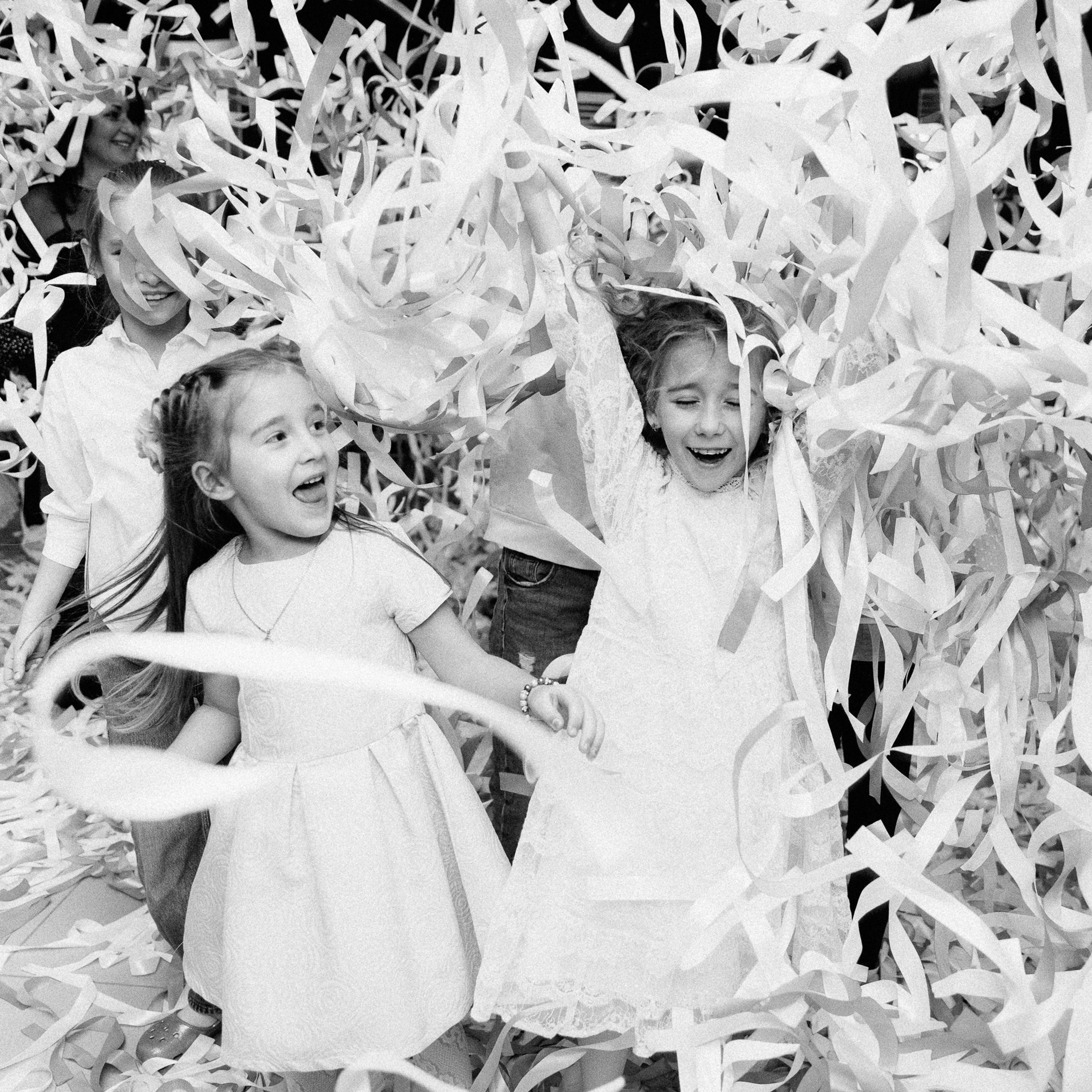 Две девочки смеются и подкидывают вверх кучу конфетти.