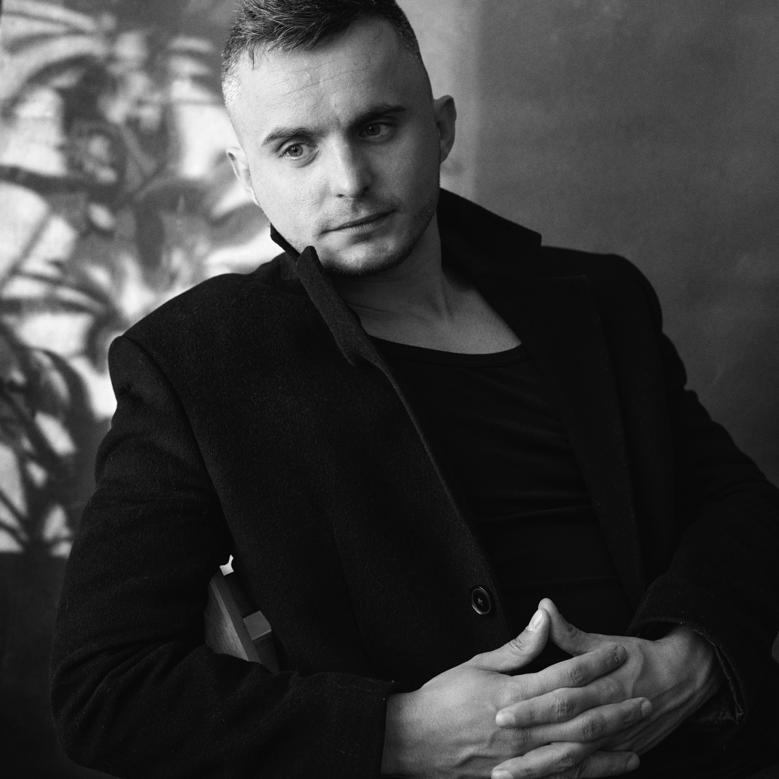 Черно- белый портрет молодого человека сидящего на стуле в черном пальто