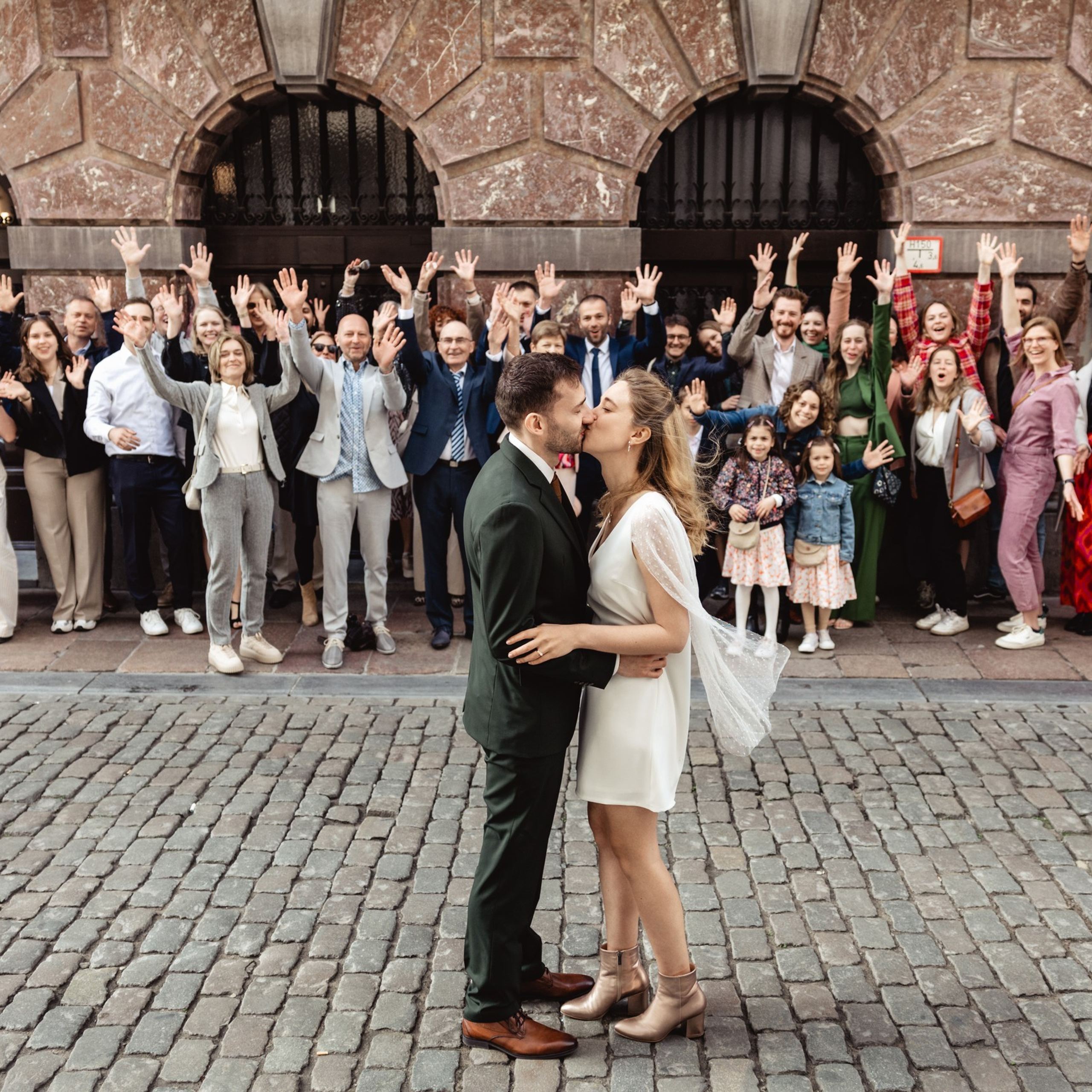 Bruidspaar staat samen op de Grote Markt met familie en gasten op de achtergrond